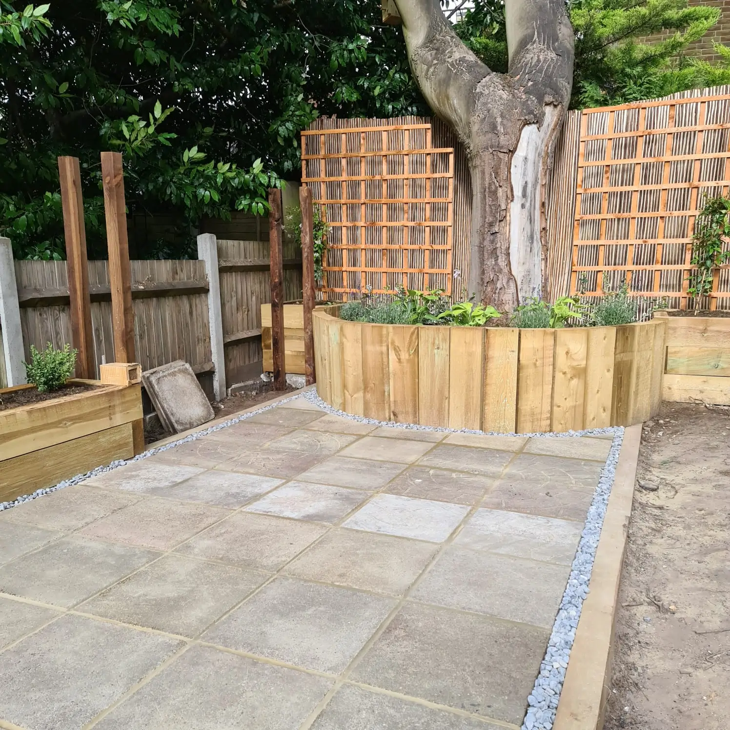 A newly paved outdoor area surrounded by wooden fencing and a tree in the background.