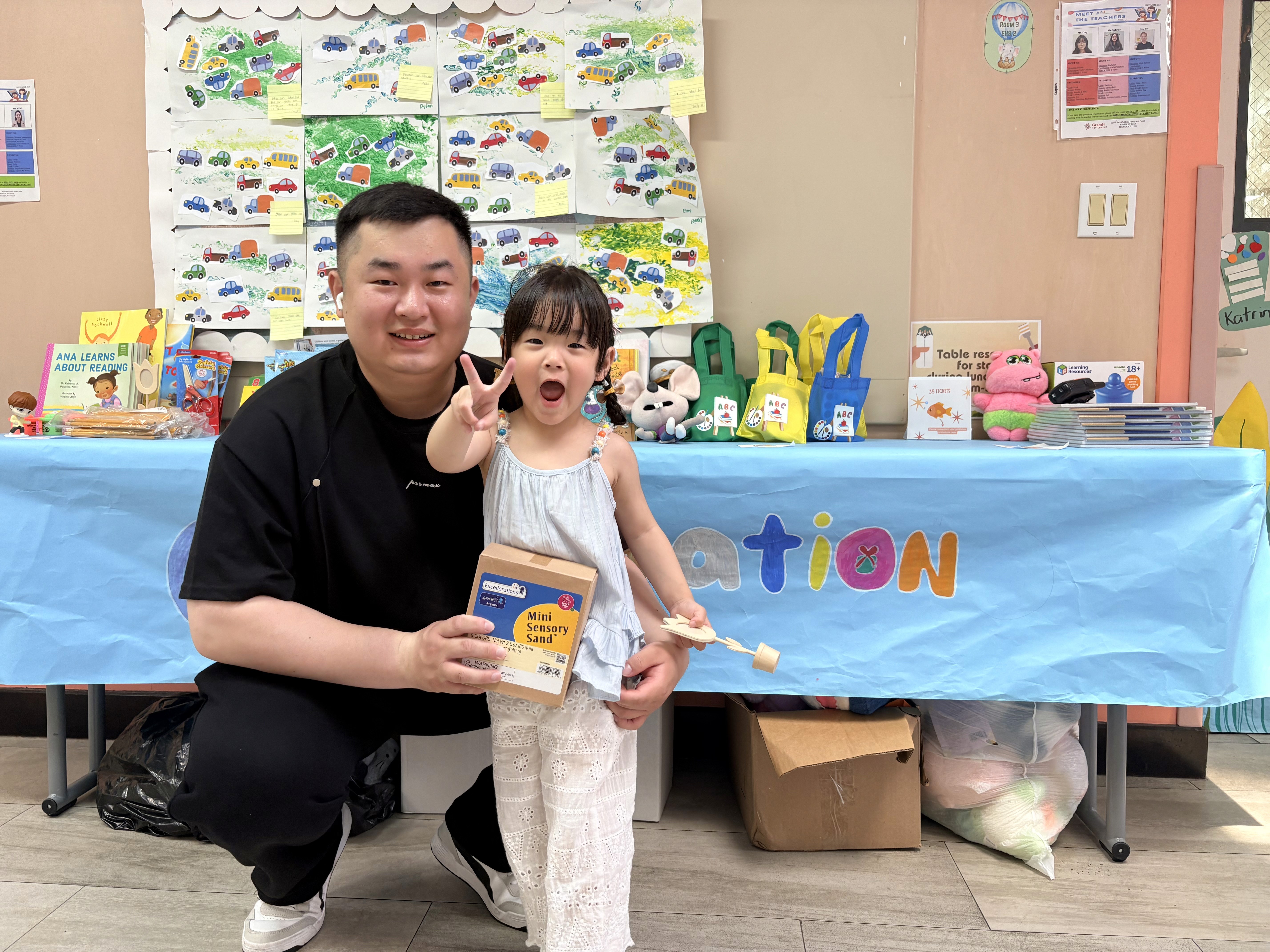 A girl poses with her father holding Sensory Sand in front of a table filled with goodies and resources.