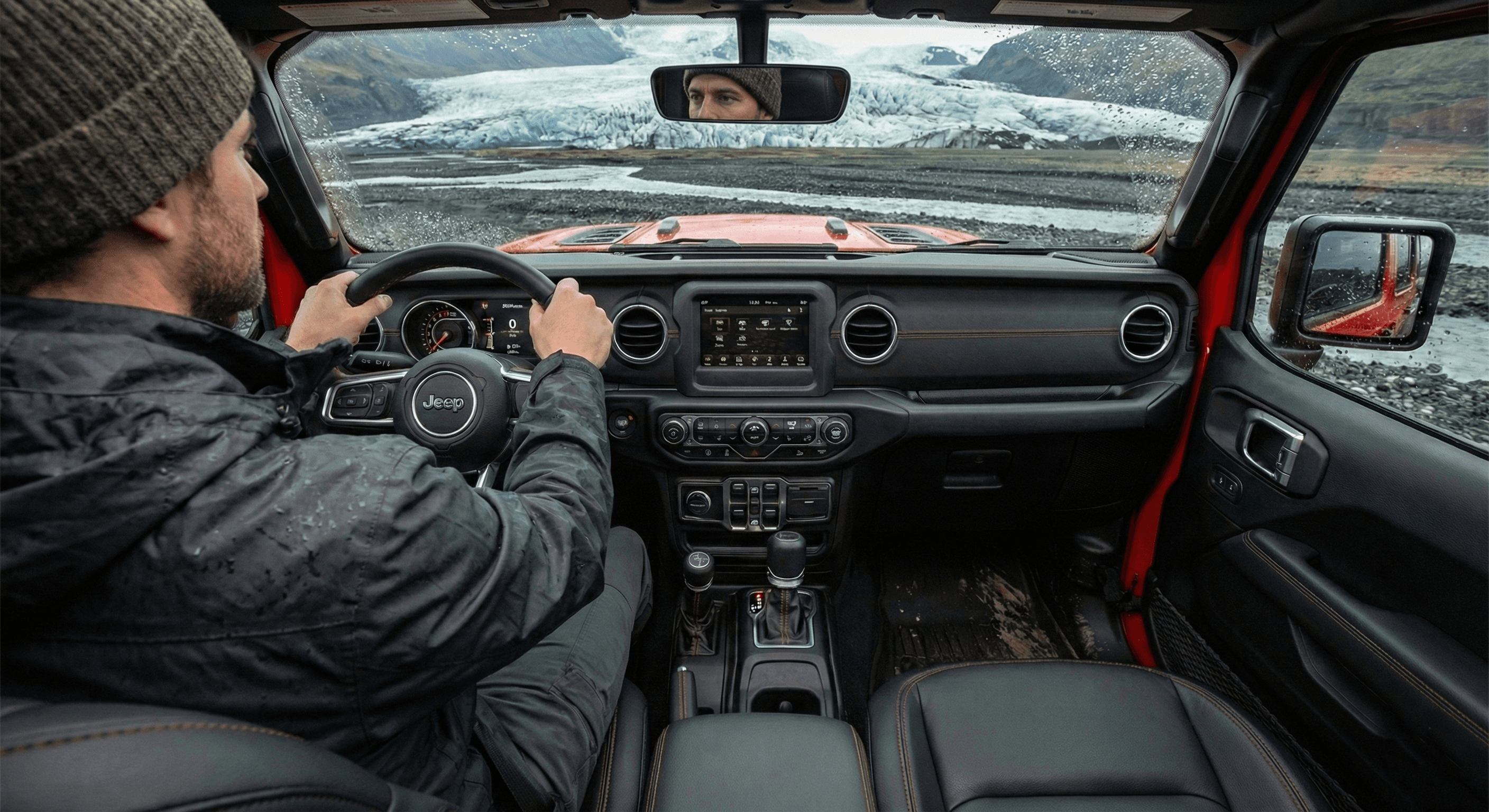 View from the driver's seat looking out through the windshield at a rocky river crossing.