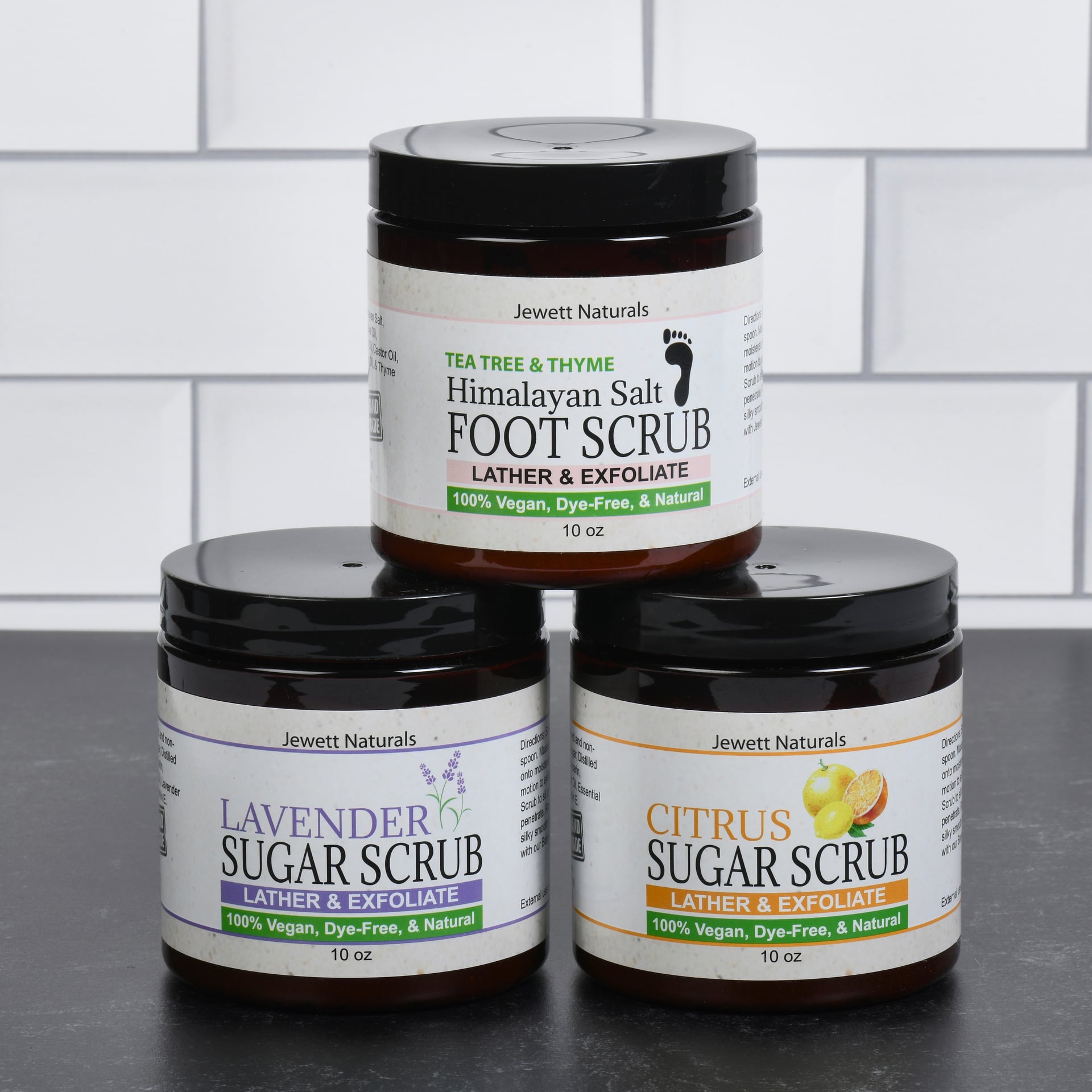 product photography of body scrub jars stacked on white tile background