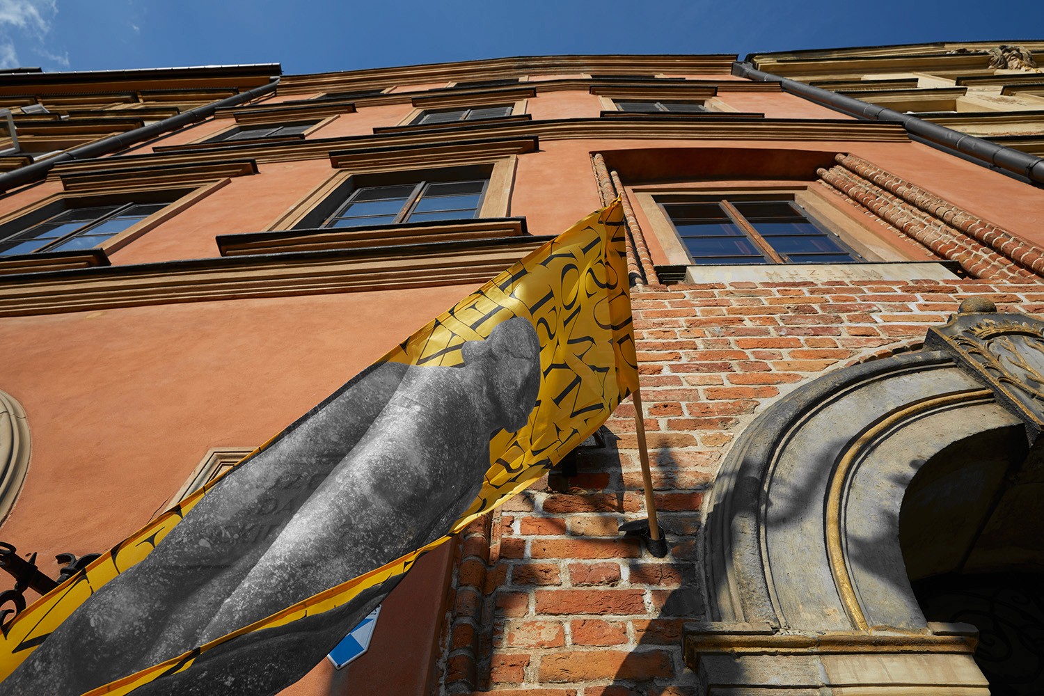 A dynamic, low-angle shot of a yellow exhibition banner against the historic facade of the Adam Mickiewicz Museum of Literature. This visual highlights the studio's ability to integrate modern typographic systems into classical urban environments.