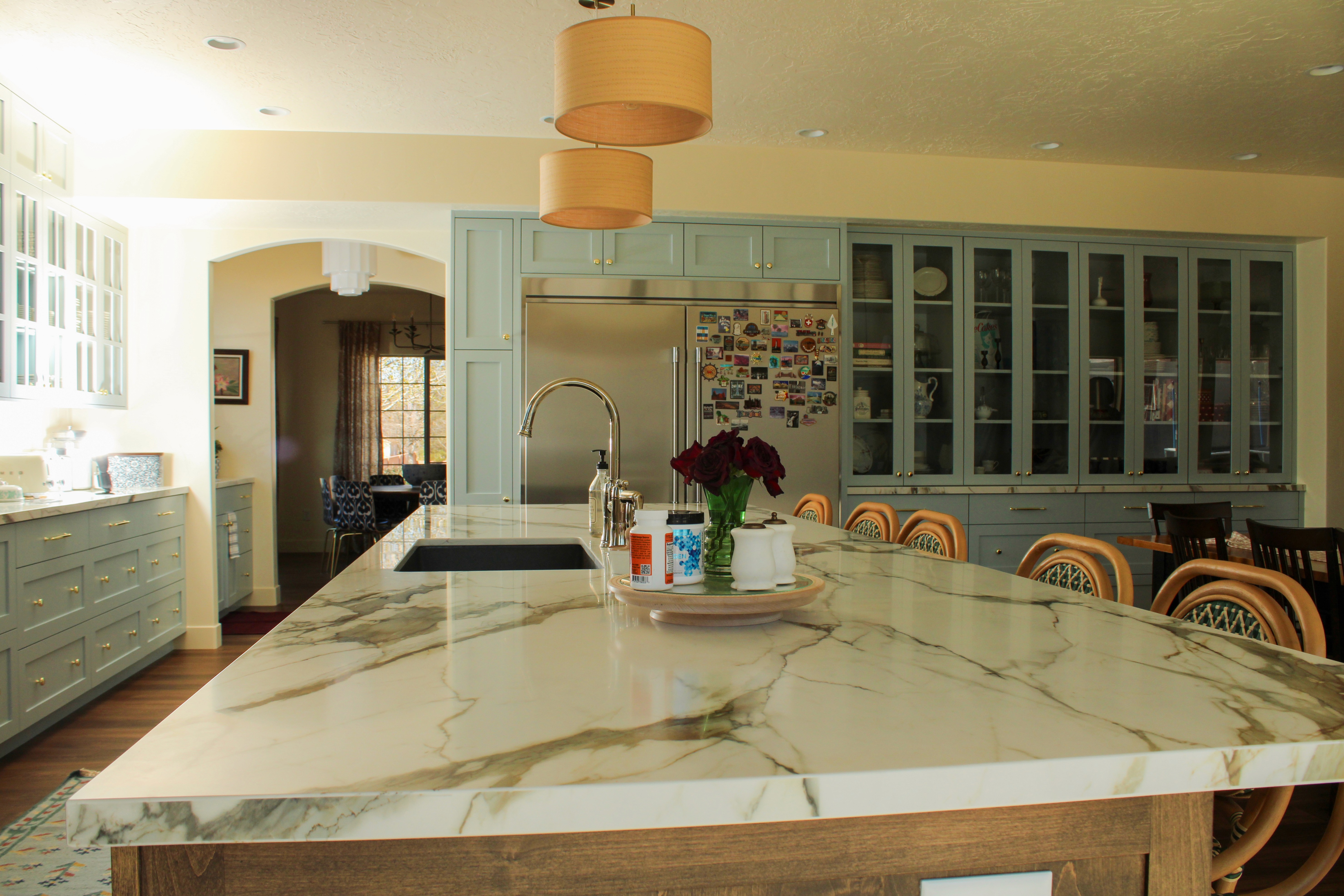 View over the kitchen island toward a wall of pale blue cabinets with glass doors and a double fridge in a Washington, Utah remodel, combining style and functionality