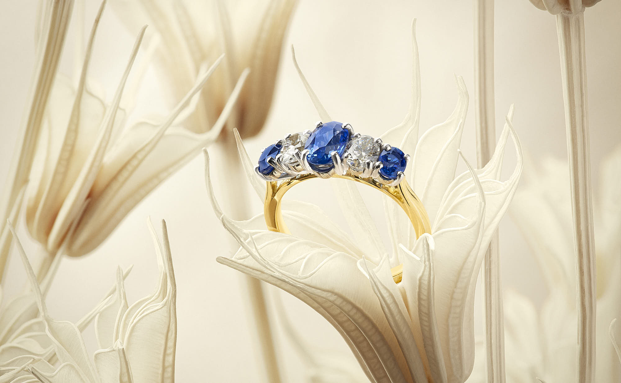 A close-up of a gold ring with blue gemstones, displayed against a soft, neutral background.