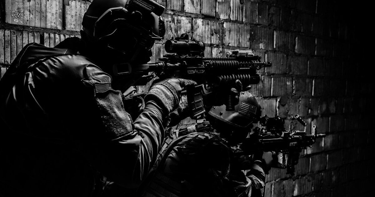 Dark tones of deep blue photo close-up of 2 armed soldiers of a small unit pointing to unknown threat in front of them.