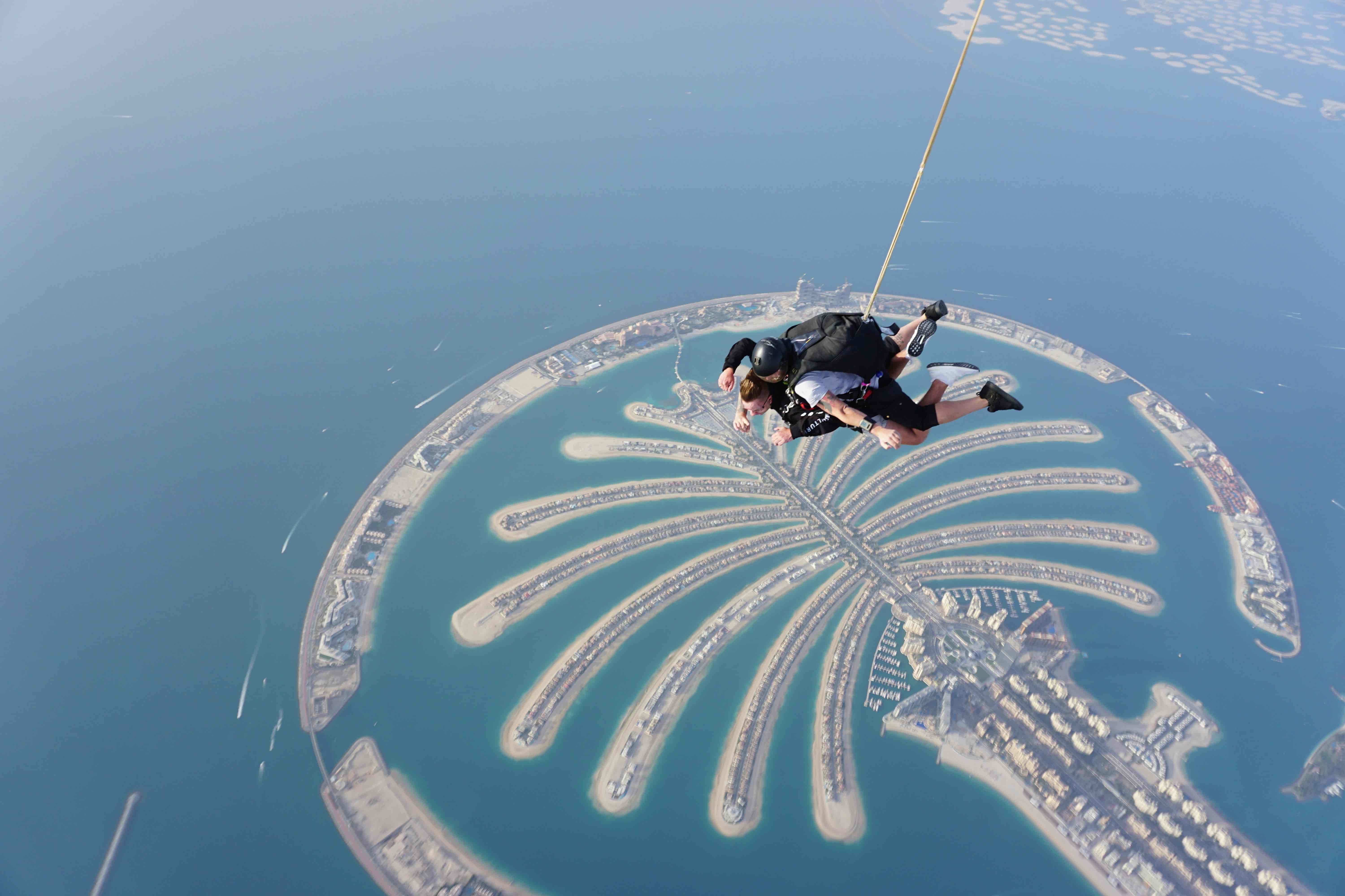 Skydivers free-falling above Palm Jumeirah in Dubai with a clear aerial view of the island’s palm-shaped design.