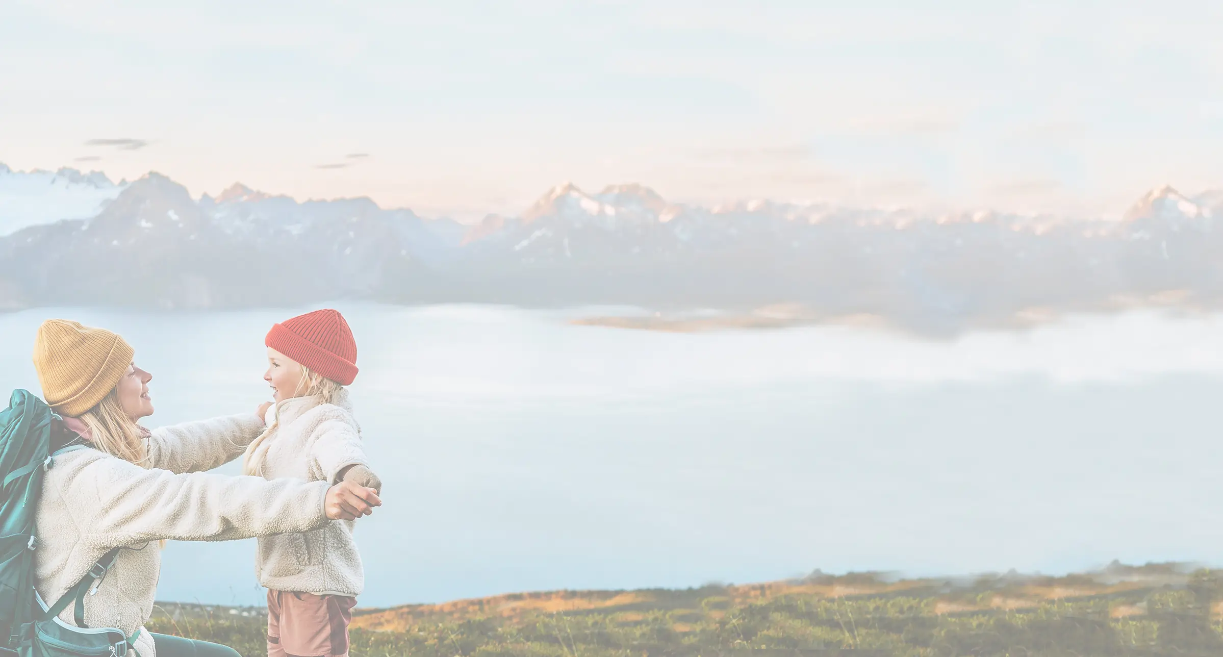 Mother and daughter outdoors, hiking near a large lake with mountains in the background.