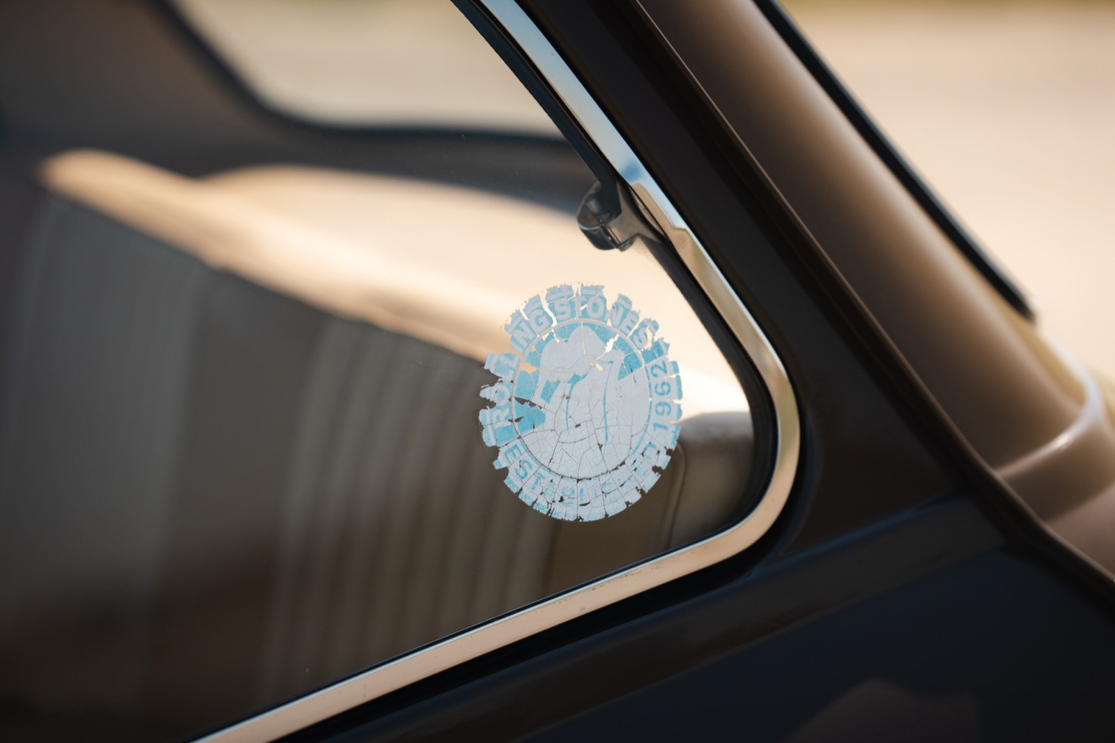 A close-up of a circular sticker on a car window, with soft sunlight reflecting off the glass surface.