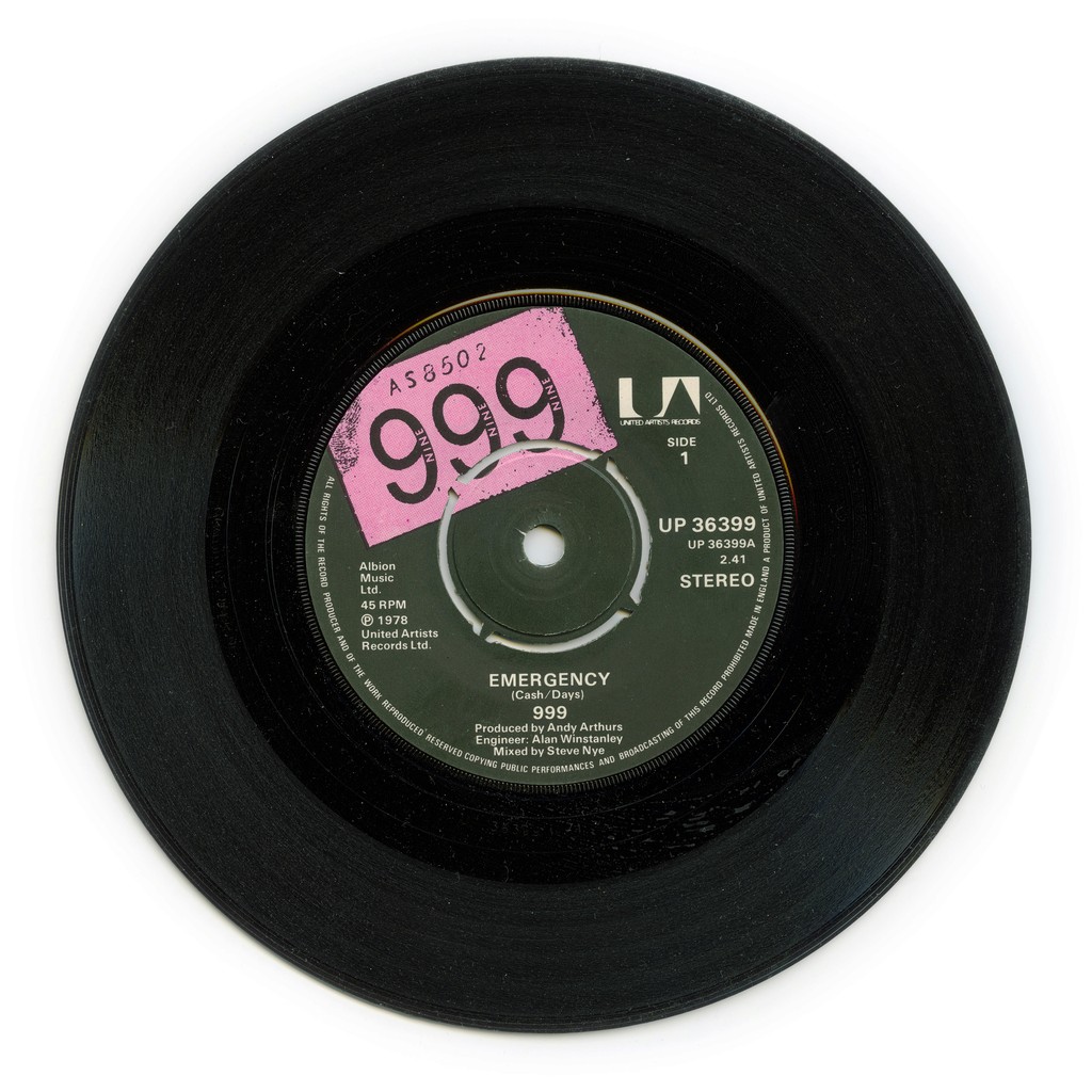 The image features a vintage 7-inch vinyl record of the single "Emergency" by the band 999, released in 1978 by United Artists Records. The record's label includes essential details such as the band's name, song title, and production credits, with a notable pink sticker displaying the price, enhancing its retro appeal for collectors and music enthusiasts.