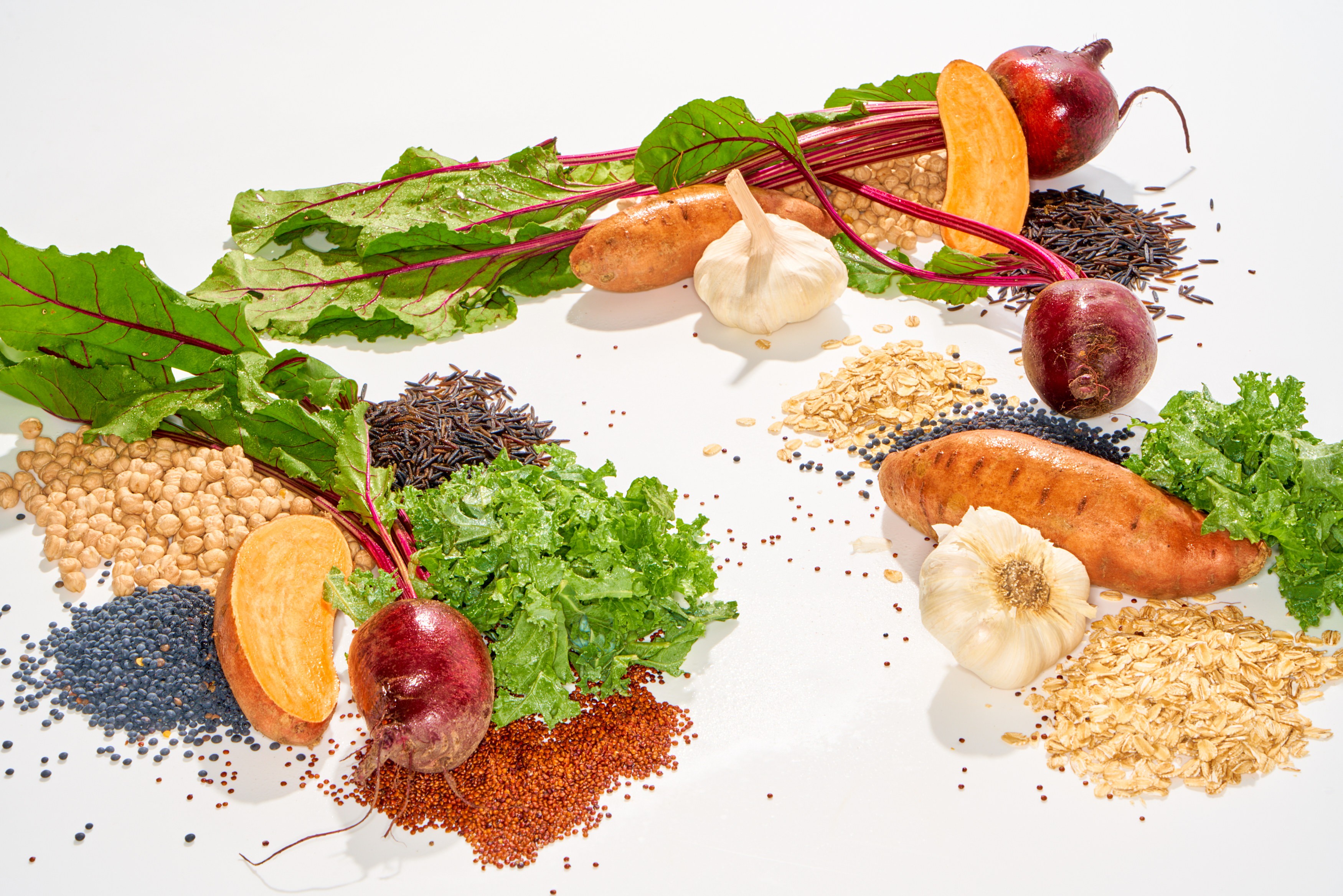 Graphic food still life with beets greens grains garlic and sweet potatoes