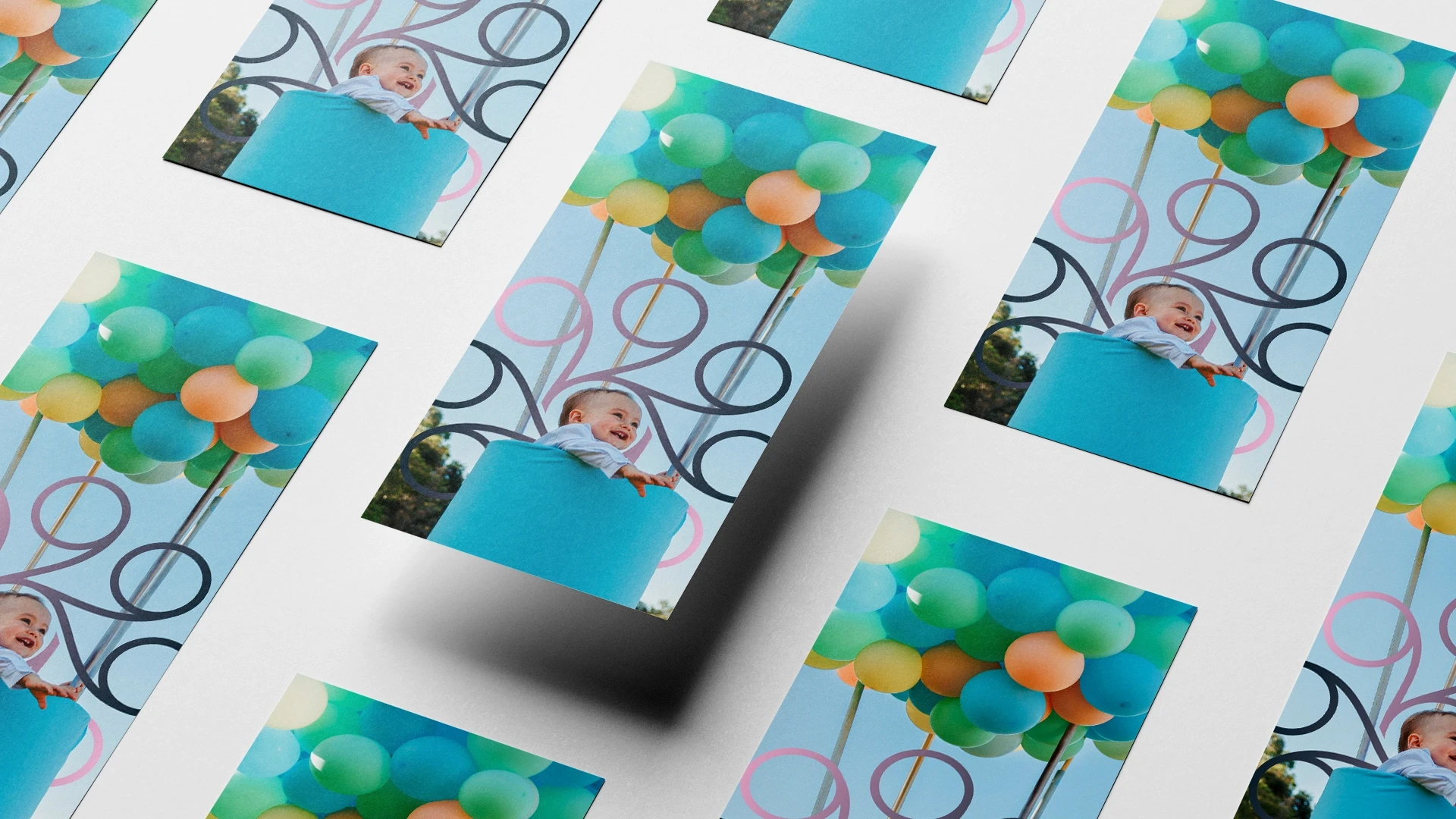 Disposição em perspectiva de cartões promocionais e fotos impressas de ensaio fotográfico infantil, mostrando um bebê sorrindo dentro de um cesto decorativo azul com balões coloridos.