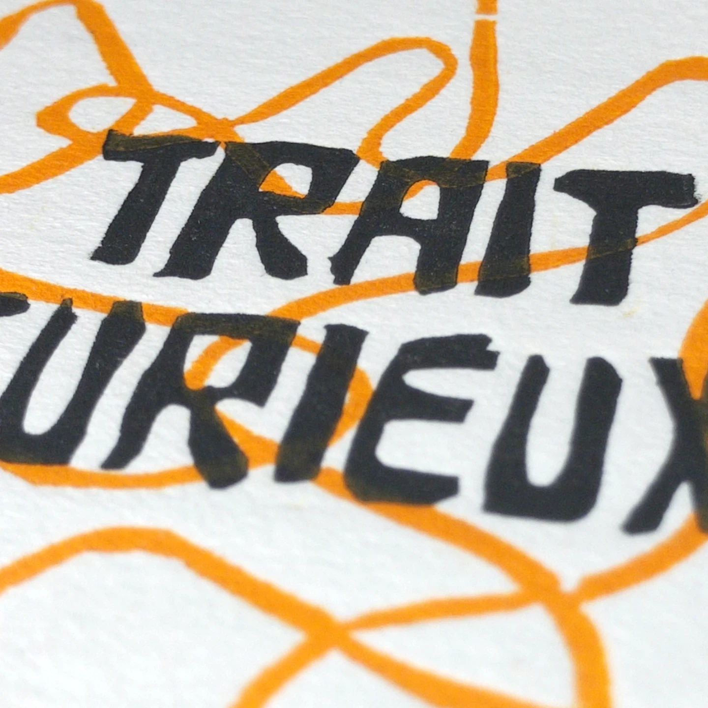 Gros plan sur le lettrage « Trait Curieux » gravé à la main et imprimé en noir par-dessus des traits orange, sur papier blanc texturé.