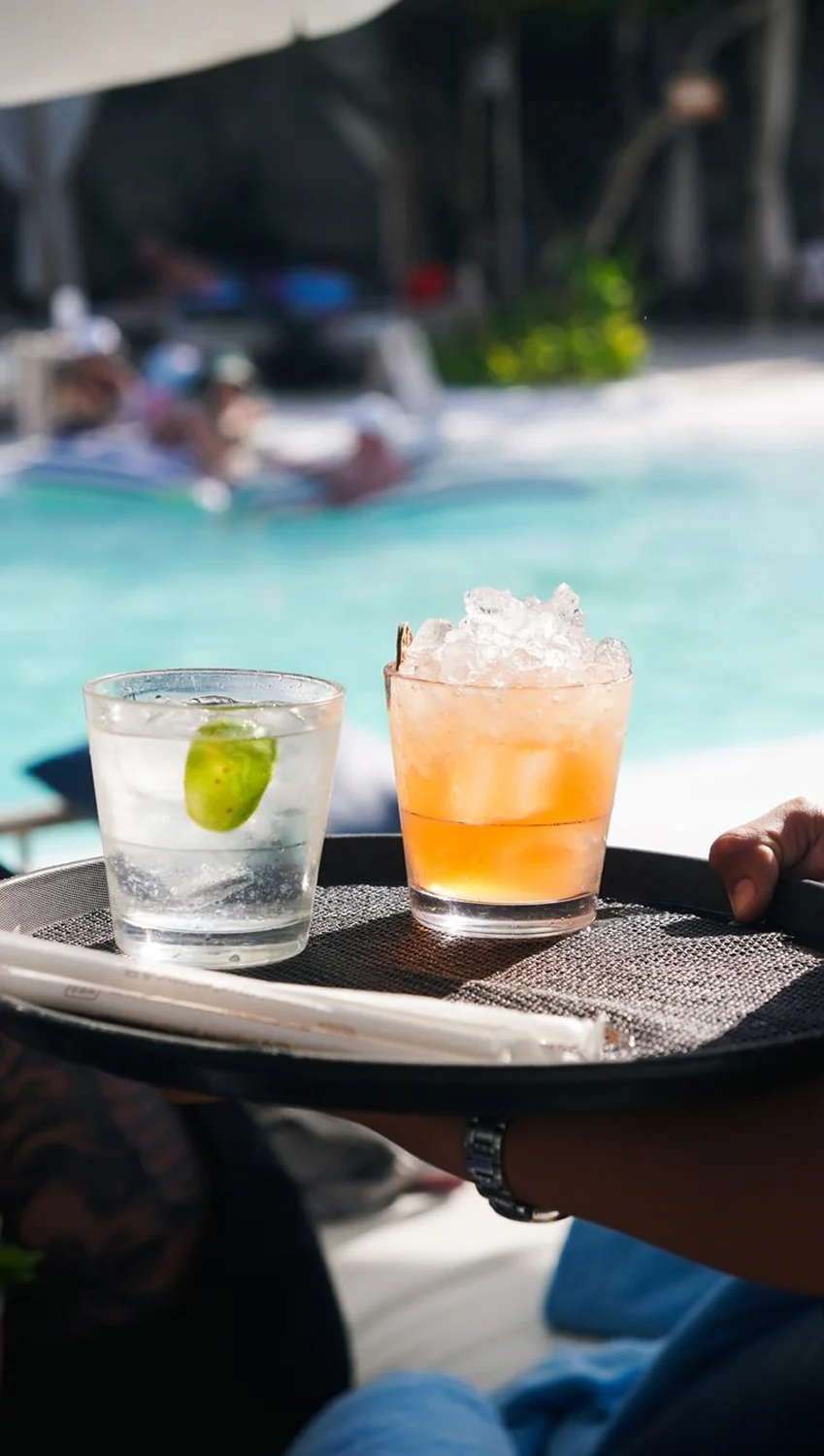 Poolside drinks served on a tray beside a swimming pool with guests relaxing in the background.