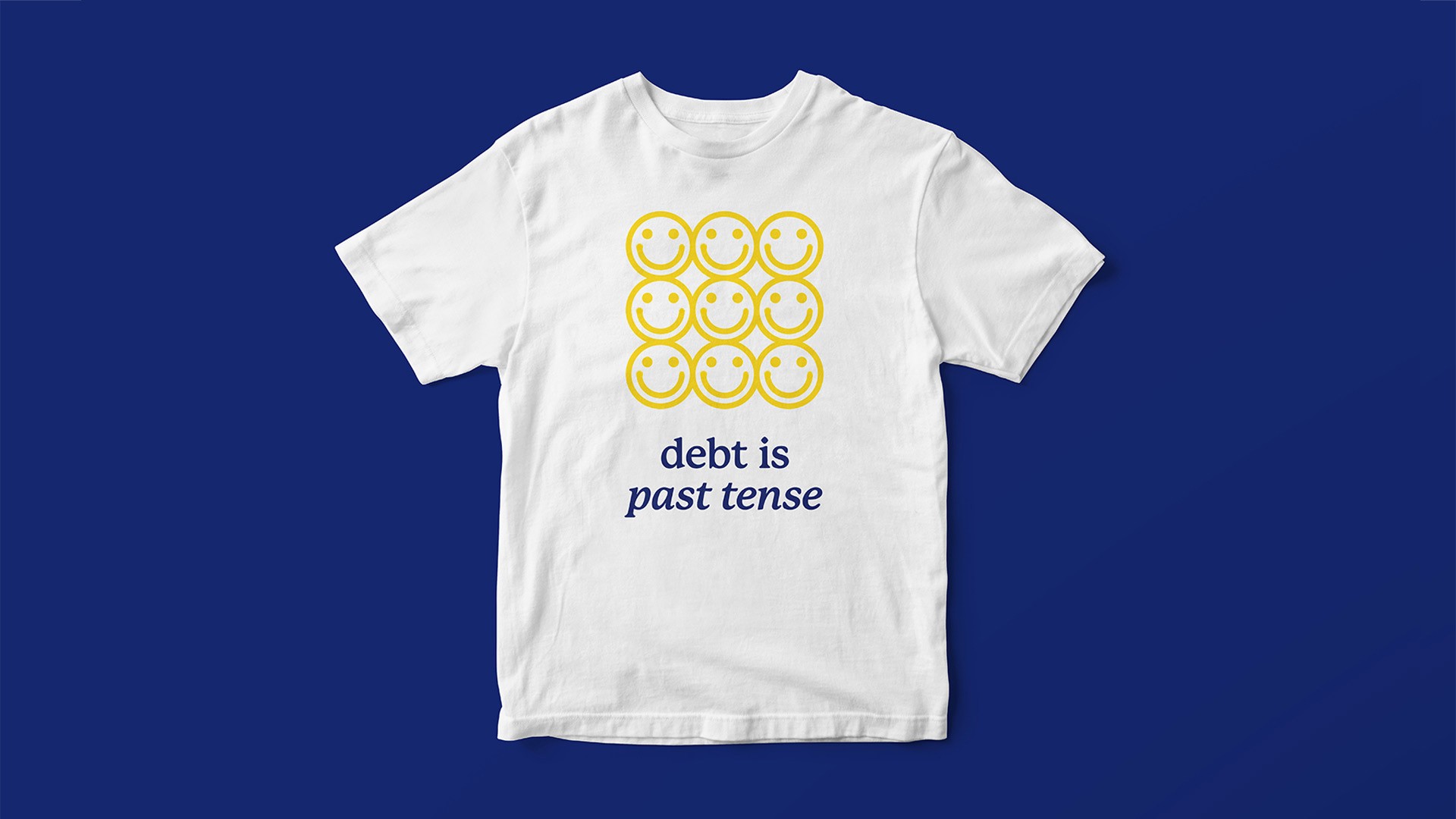 A white t-shirt with short sleeves and a crew neck lies flat against a solid dark blue background. Centered on the shirt is a grid of nine yellow smiley faces arranged in three rows of three. Below the smiley faces, the text "debt is past tense" is printed in dark blue.
