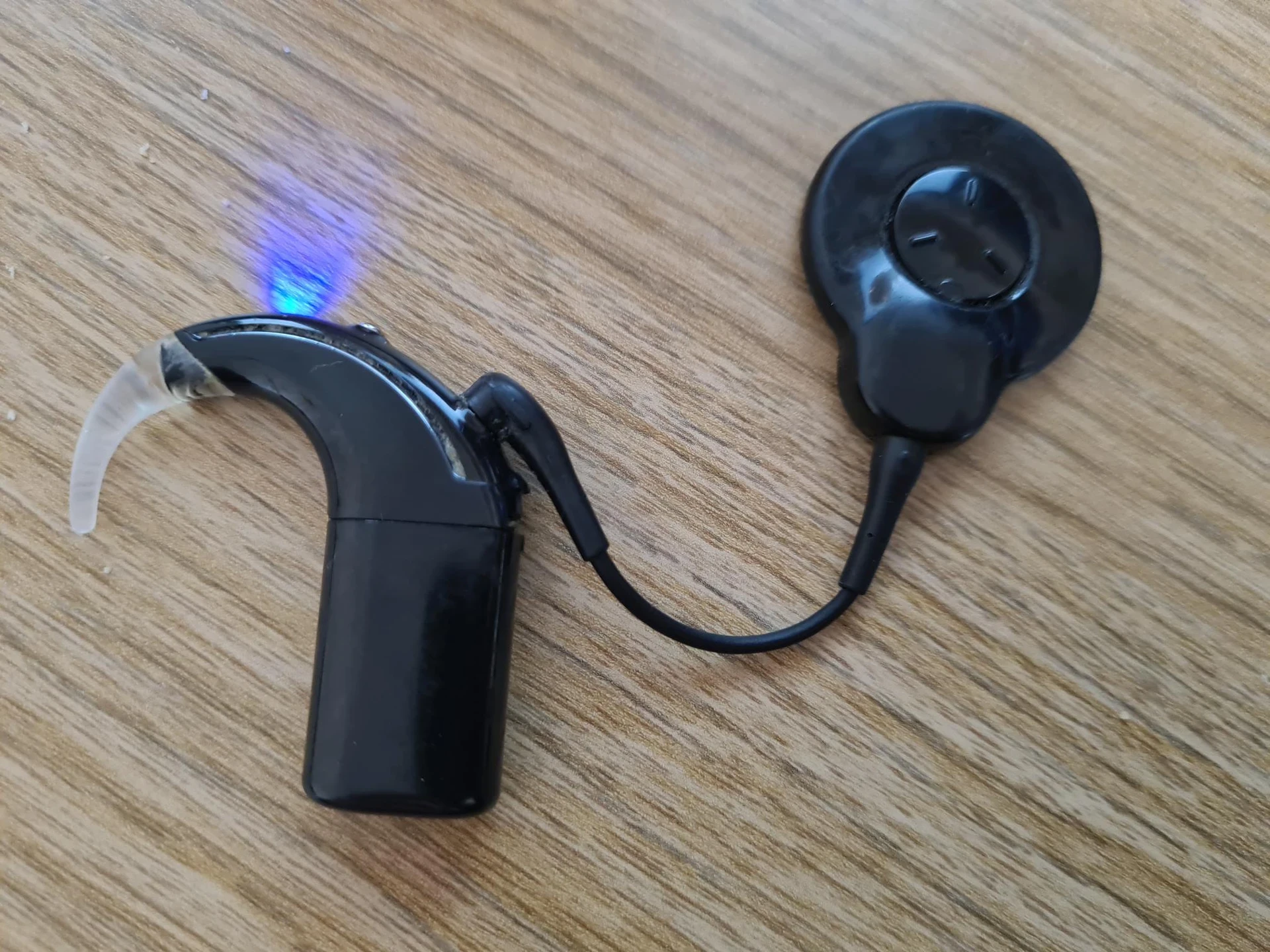 A black cochlear implant external processor photographed on a wooden surface