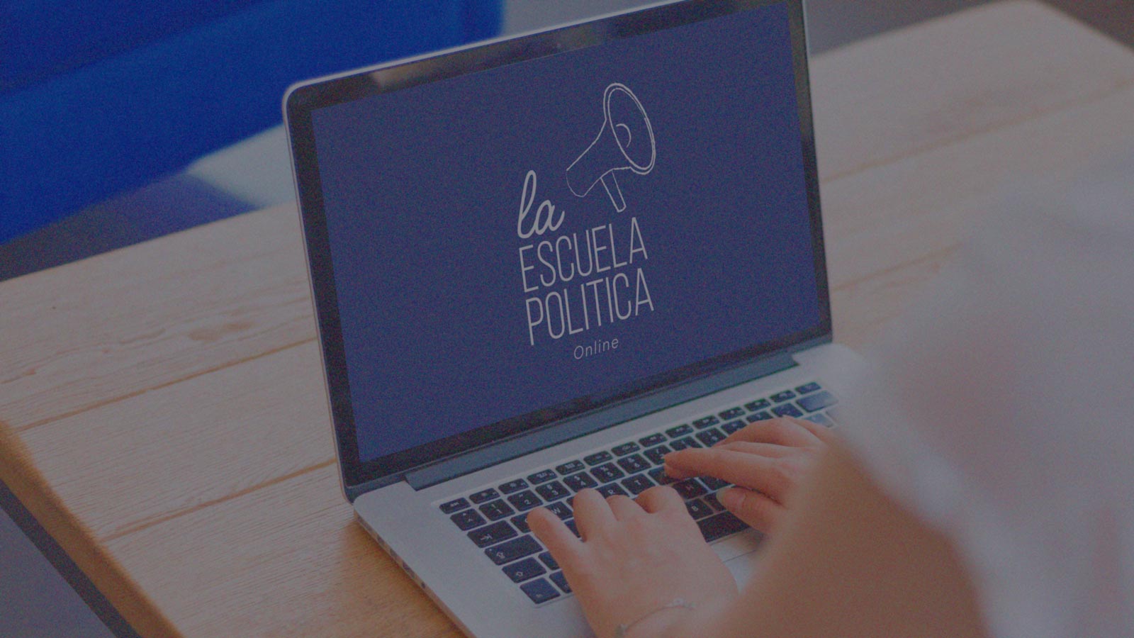 Portada de La Escuela Política - Online, programa de formación de IdeaPaís, mostrando un computador sobre una mesa mientras que en la pantalla aparece el logo de La Escuela Política. 