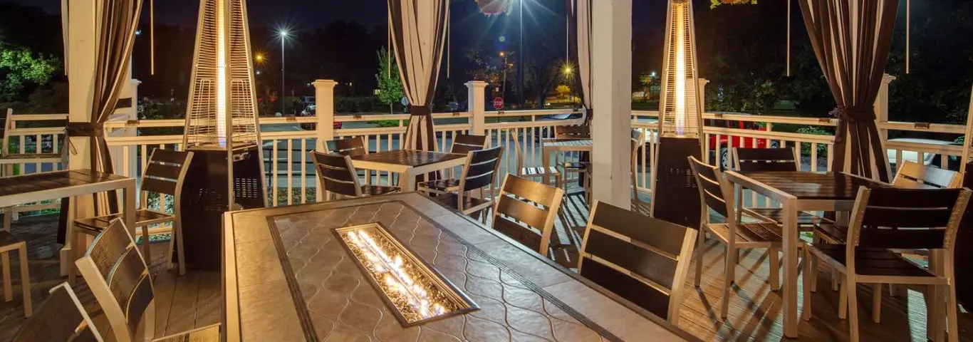 Outdoor dining patio at night with fire pit table and patio heaters.