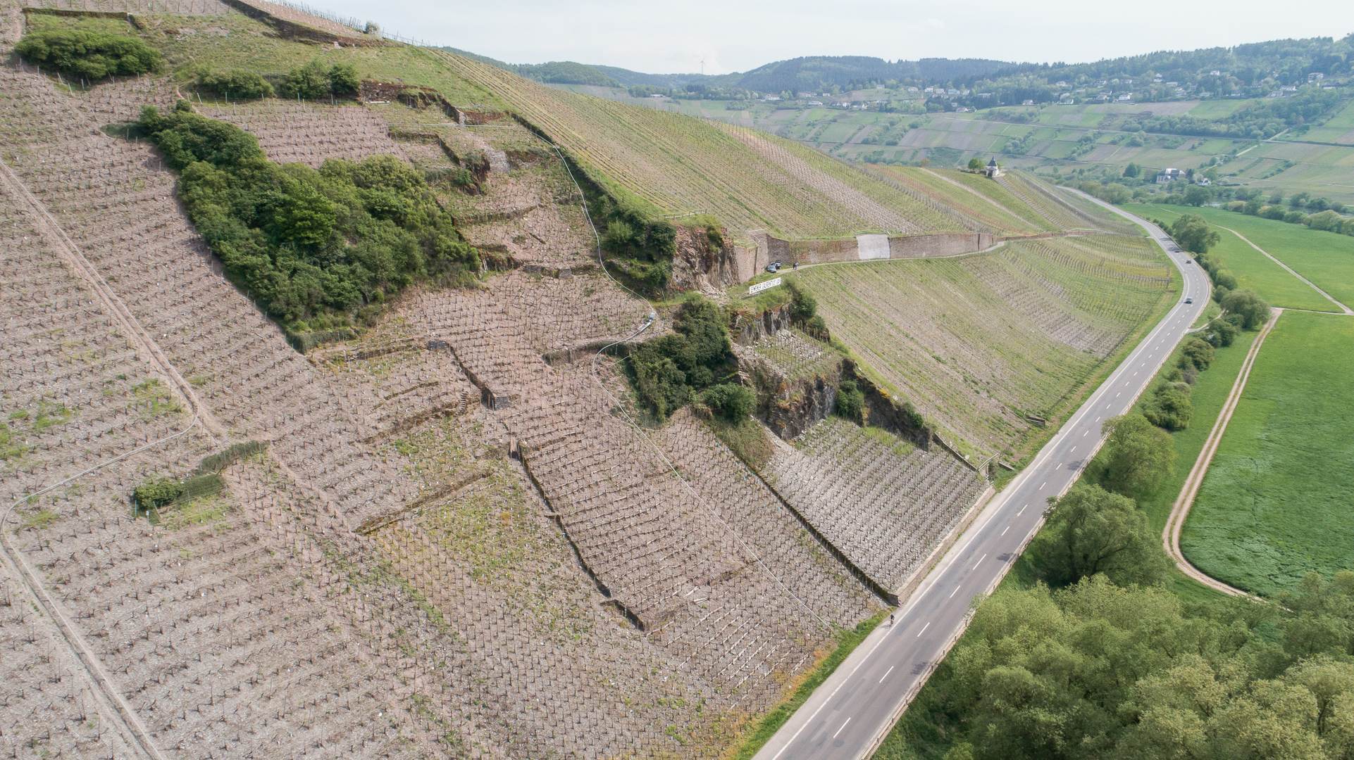 Aerial view of a hilly landscape with terraced fields and vegetation, surrounded by rolling hills.