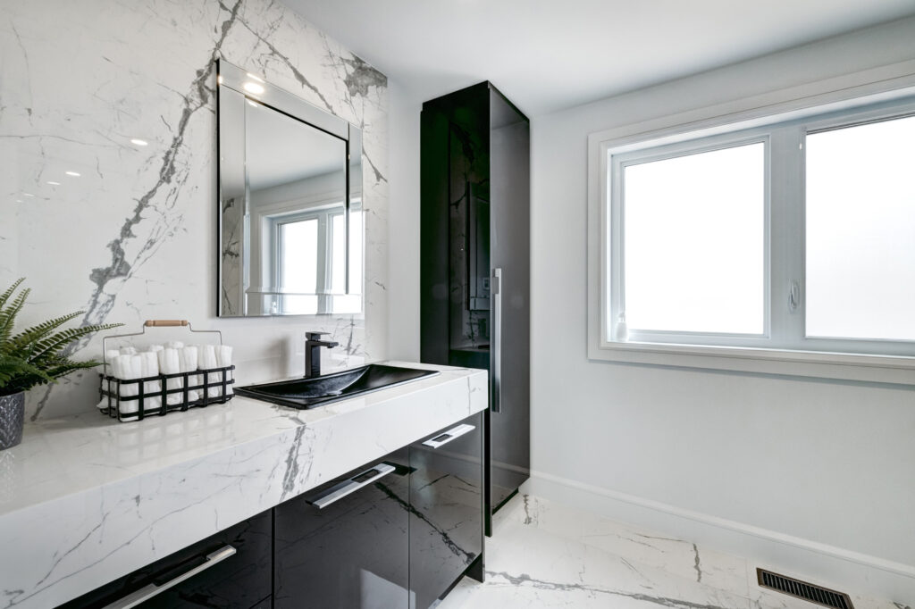 Bright open-concept kitchen and dining area with black and white marble waterfall island, sleek white cabinetry, and glass staircase, showcasing B&Y Reno Corp’s custom kitchen remodeling in a modern luxury home.