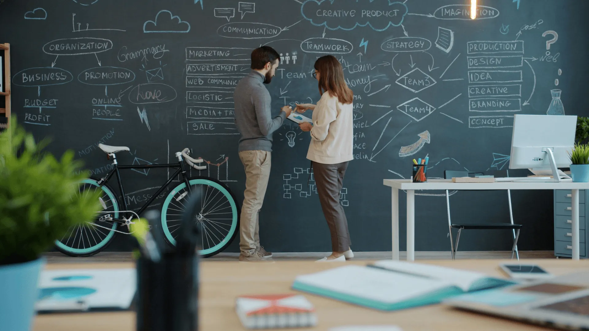 Two people stand in front of a blackboard scrawled with text and diagrams