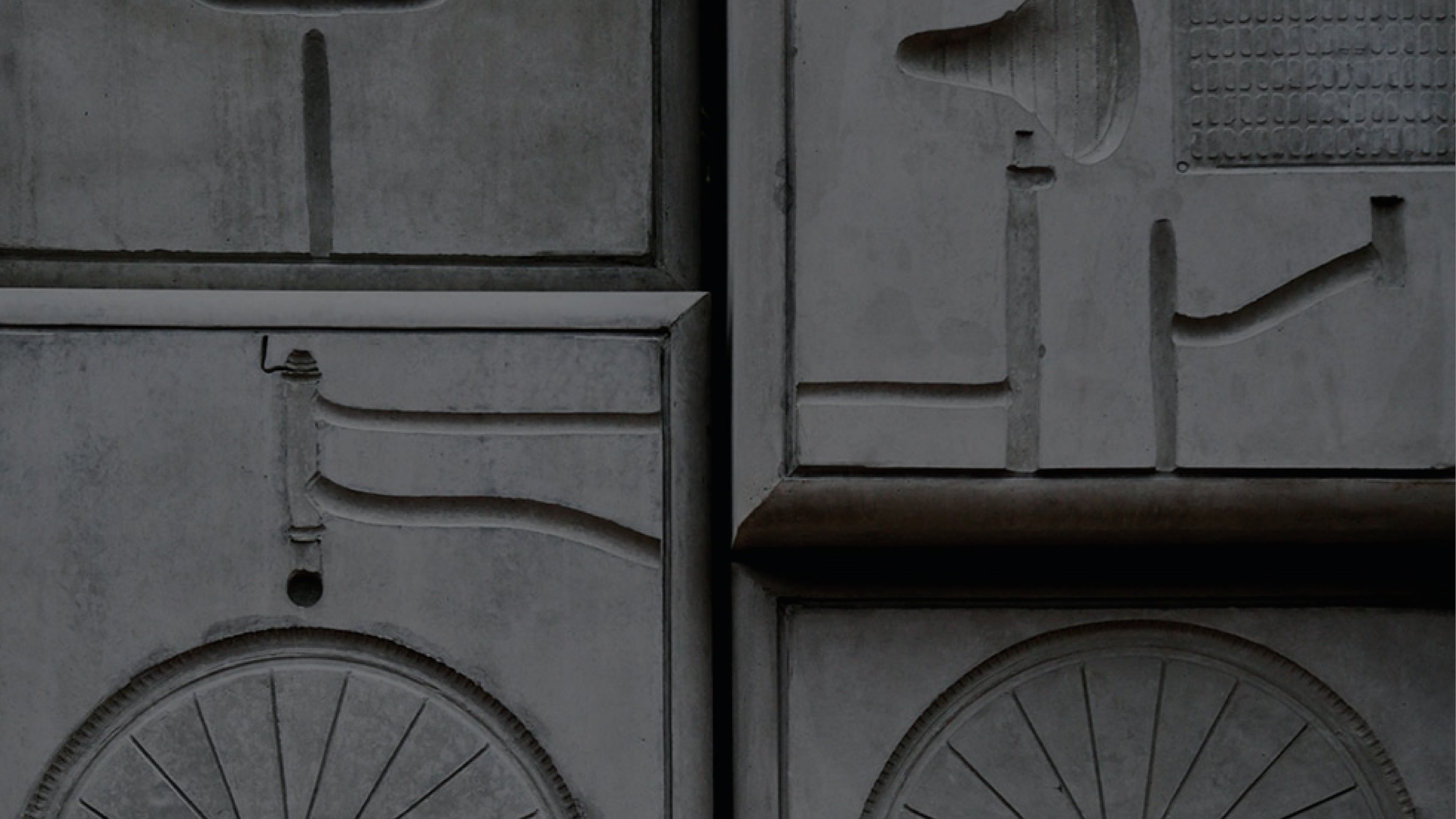 Engraved stone wall with geometric shapes and abstract figures, including circles and lines. The design is minimalist, with a somber tone.