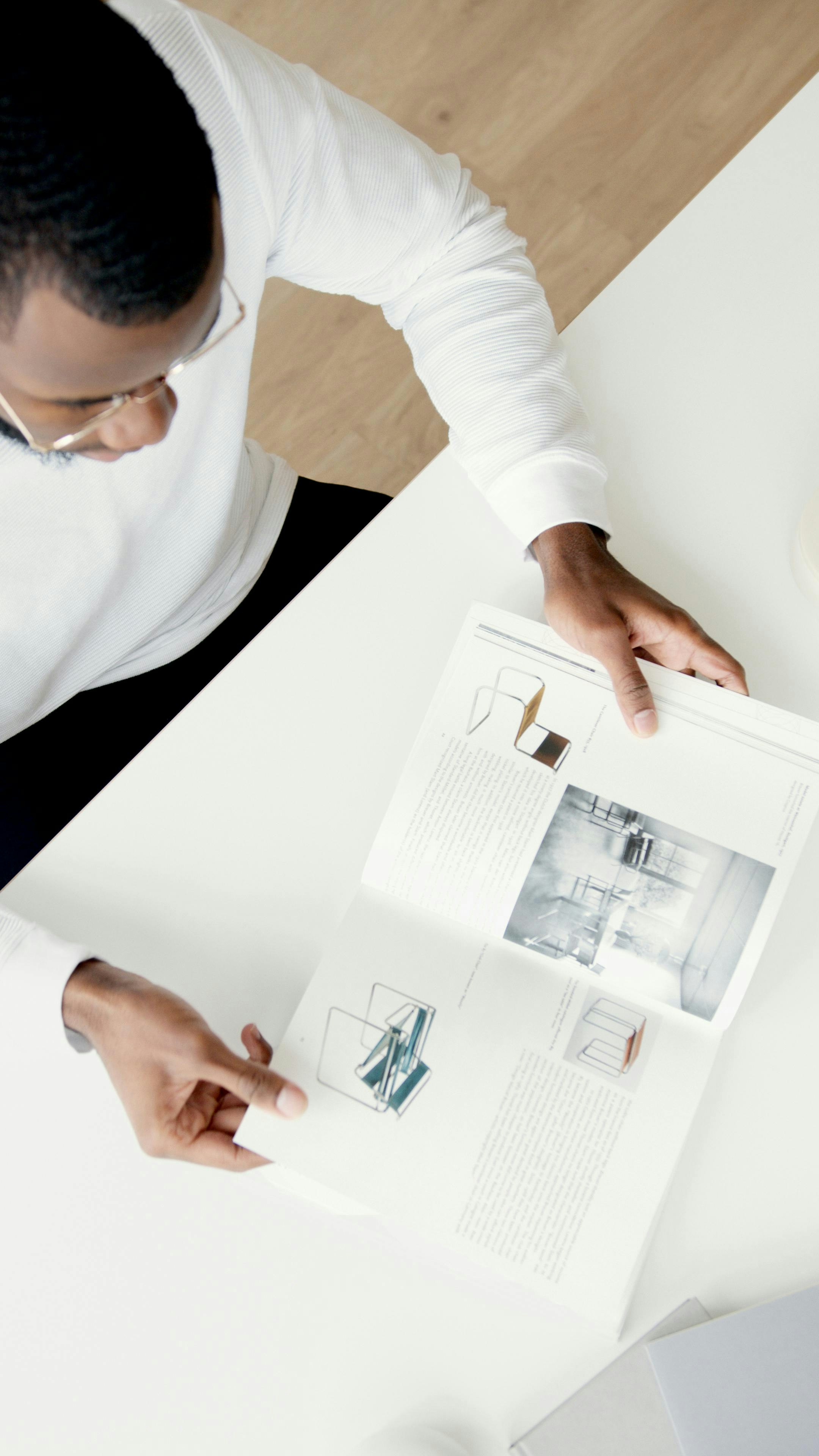 A man reads a magazine at a white table.