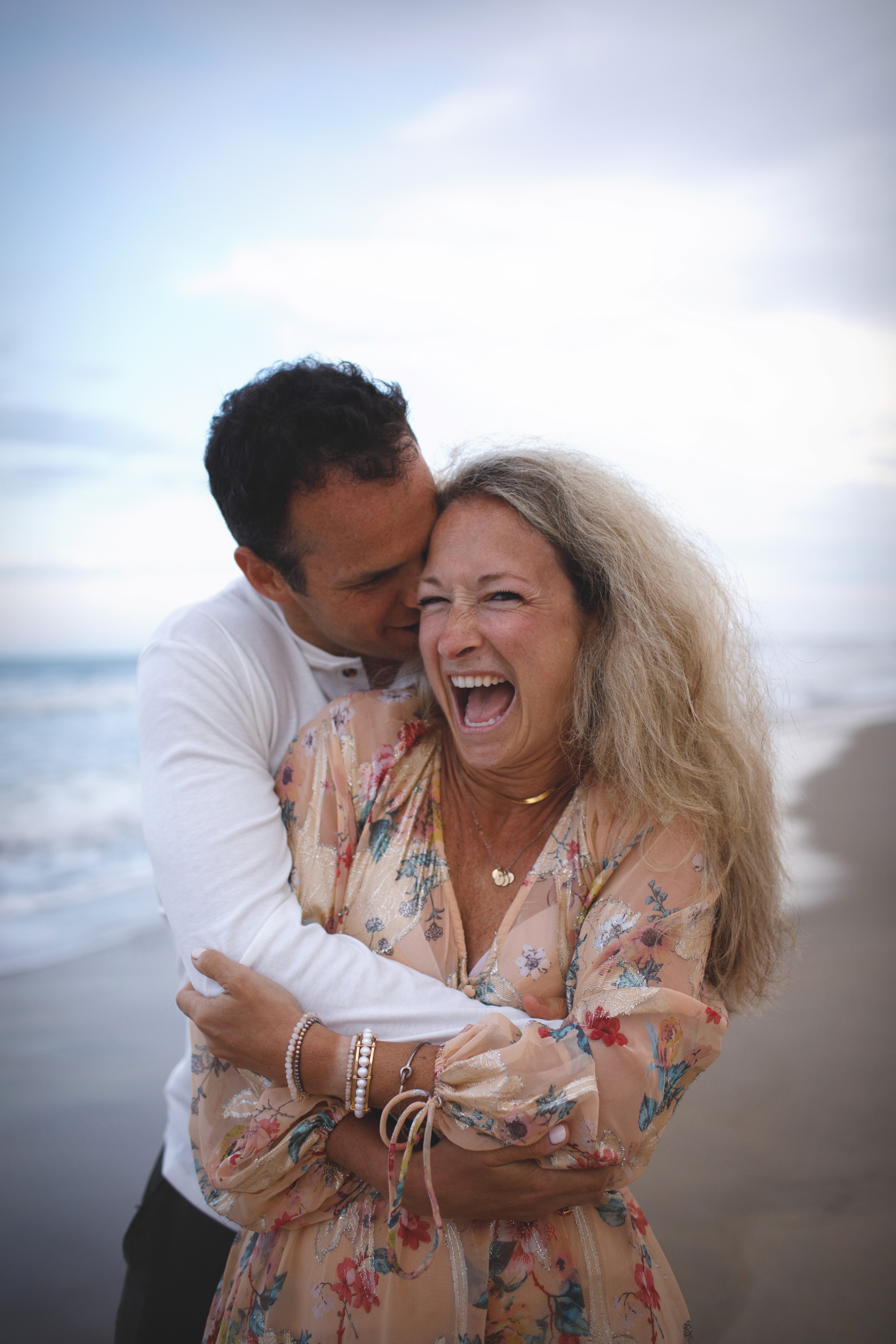 Parents holding hands and laughing while walking at the water’s edge.