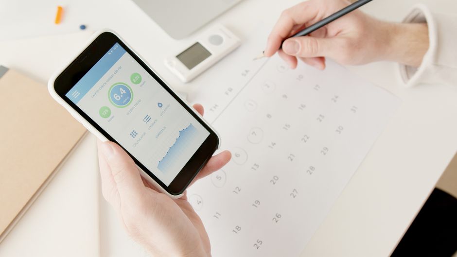 Person marking menstrual cycle dates on a calendar beside a phone.