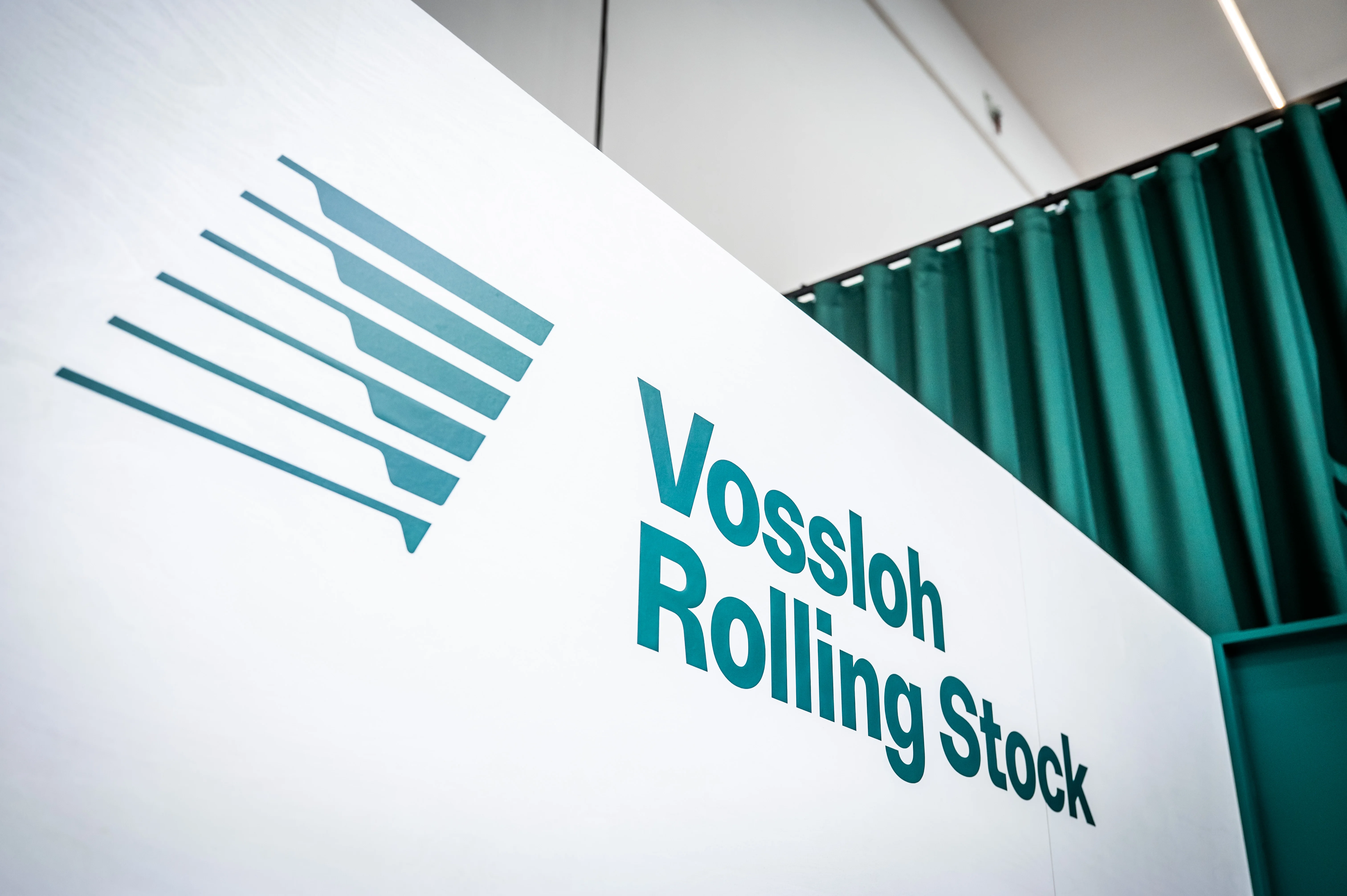 Close-up of the white Vossloh Rolling Stock counter with teal logo in front of a green curtain.