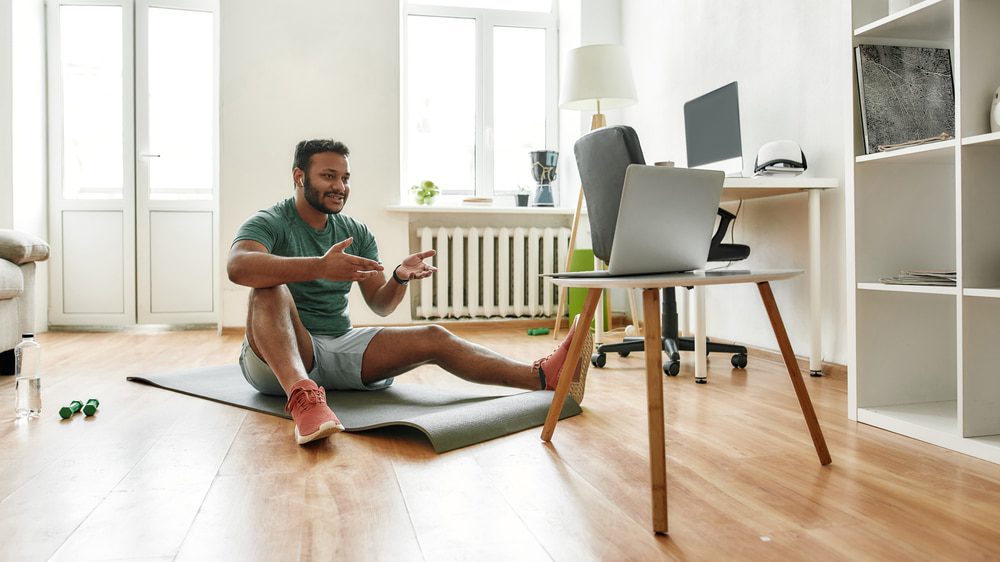 Man in athletic wear doing virtual workout at home with laptop in living room.