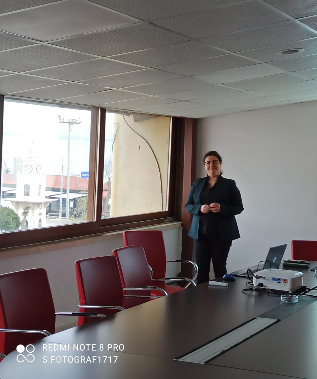 A smiling young man with crossed arms, wearing a plaid shirt and white t-shirt, poses against a dark background.