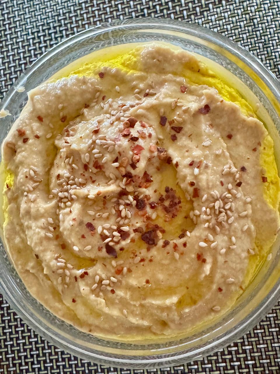 Hummus garnished with sesame seeds, chilli flakes and olive oil and served in a bowl.