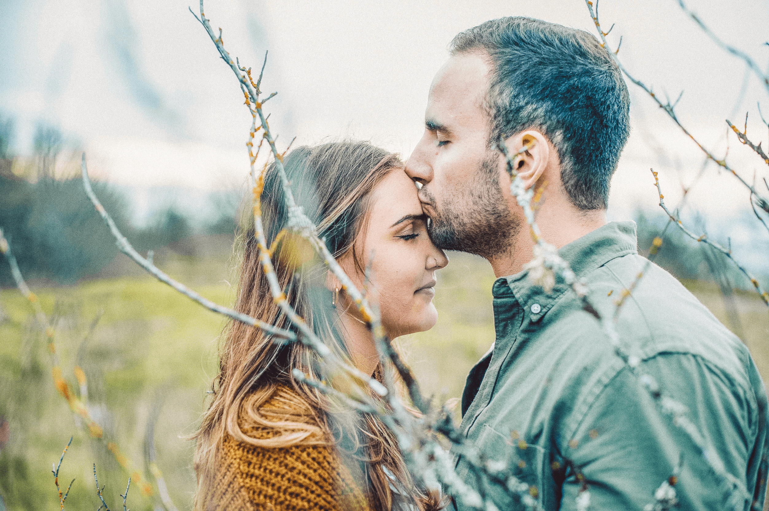 A couple sharing a tender kiss framed by soft green branches