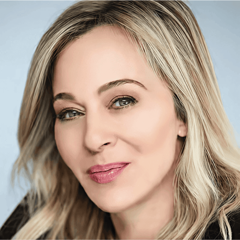 A close-up portrait of a smiling woman with long blonde hair against a light background.