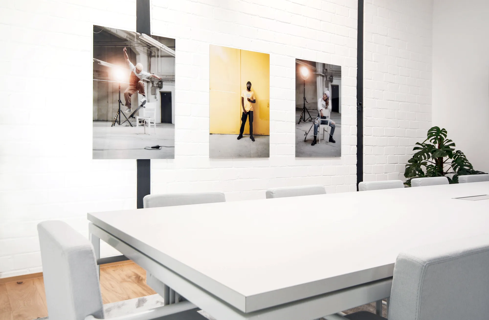 White meeting room with long table, chairs and three studio photographs on the brick wall.