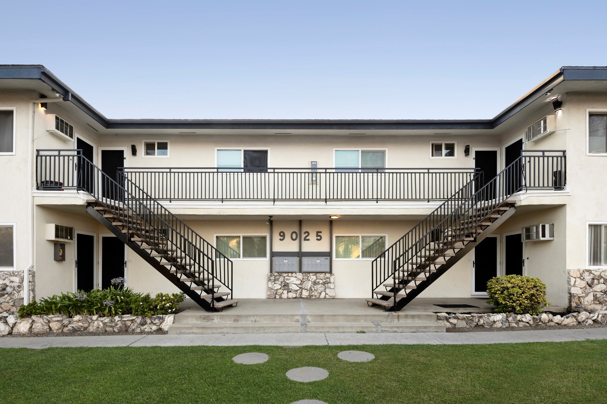 9025 Mills Avenue front elevation with dual staircases, upper walkway and stone landscape border