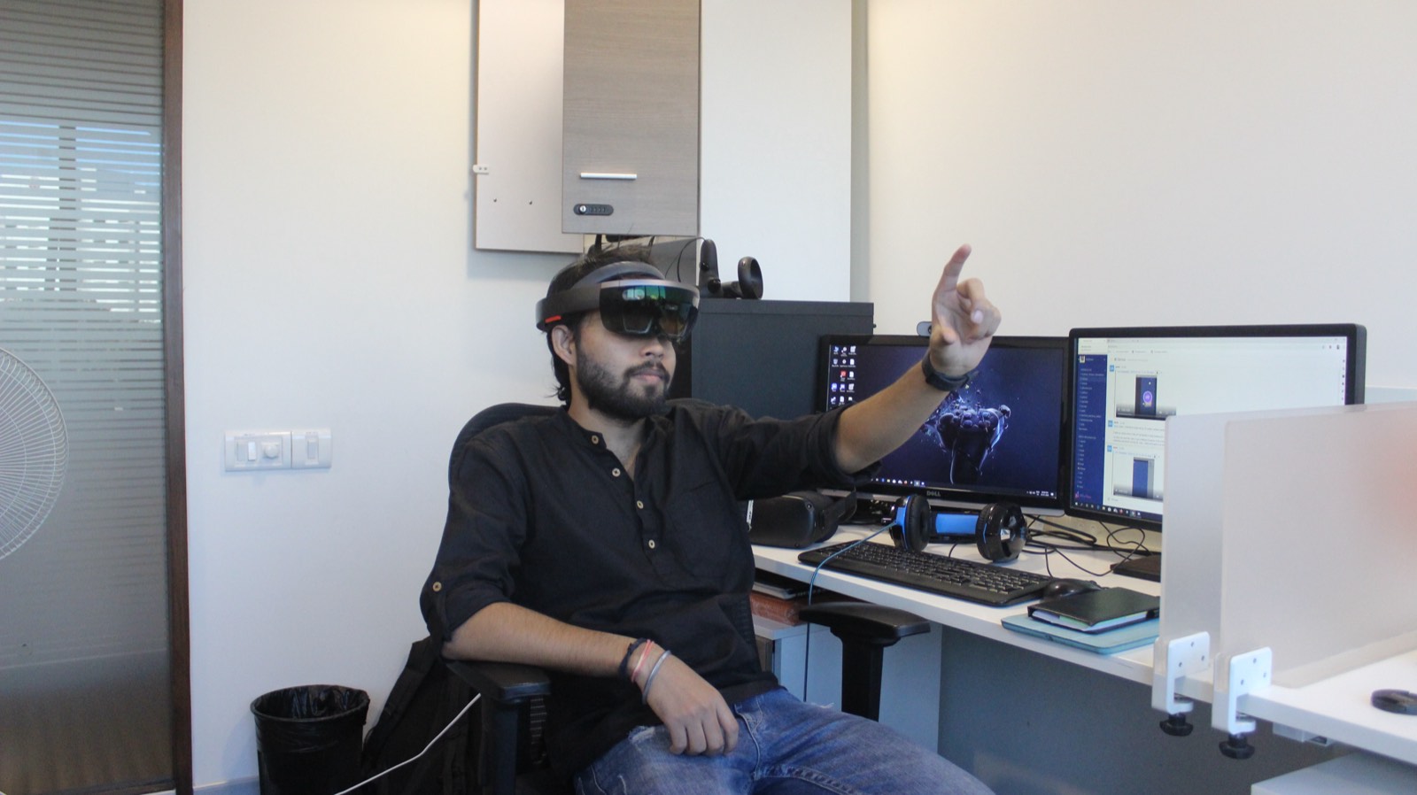 Me in a HoloLens, hand raised mid-gesture, a 3D model on the monitor behind.