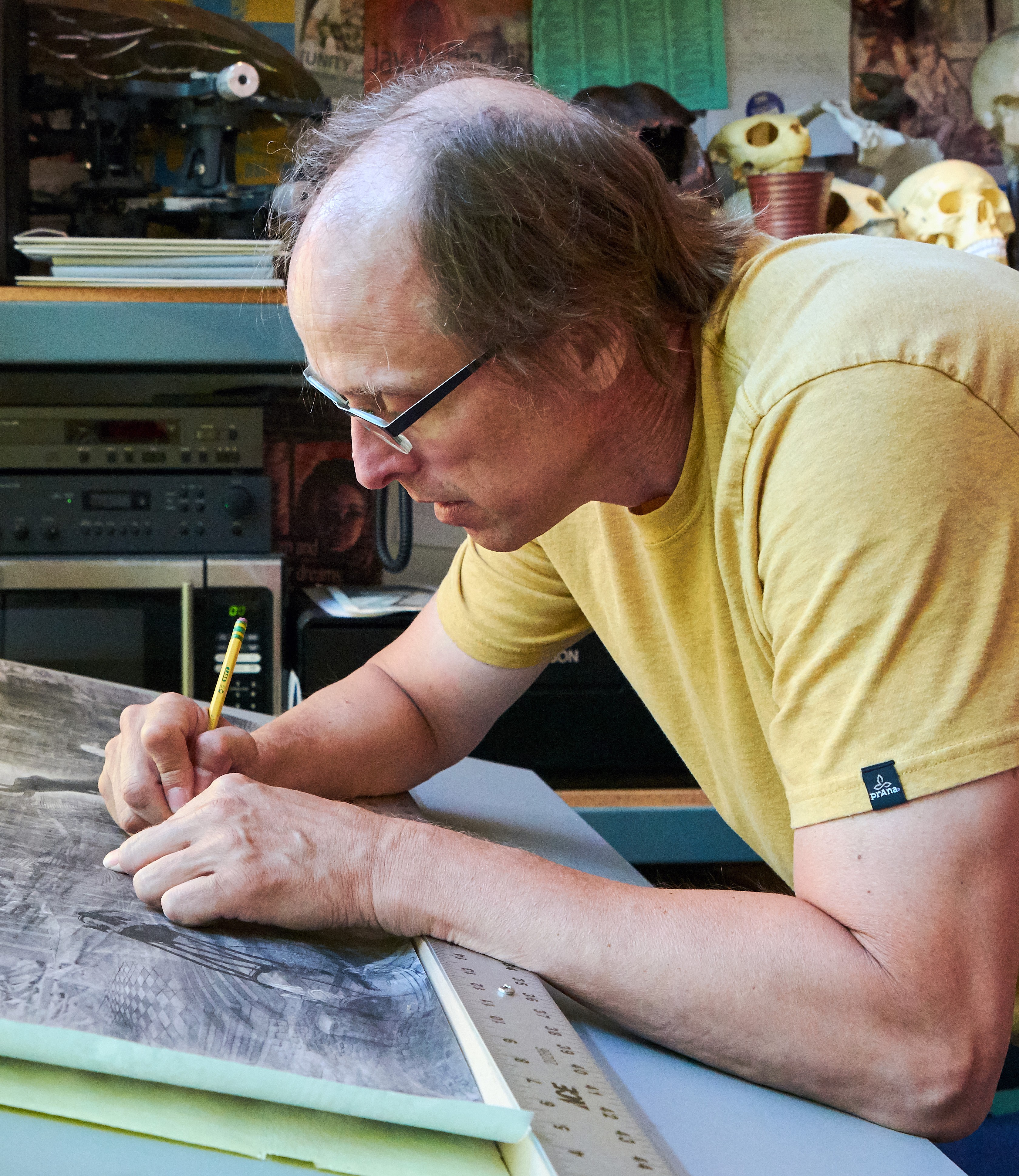 Scott Parsons, stained glass artist, bent over a design at his studio work table