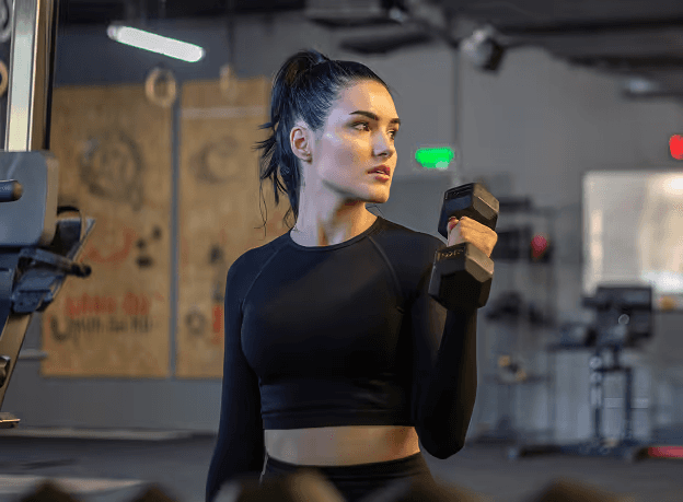 Woman in black crop top doing bicep curl with dumbbell in gym.