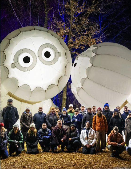 The Zauberpark Festival team posing at night in front of the giant inflatable Anooki in Zurich