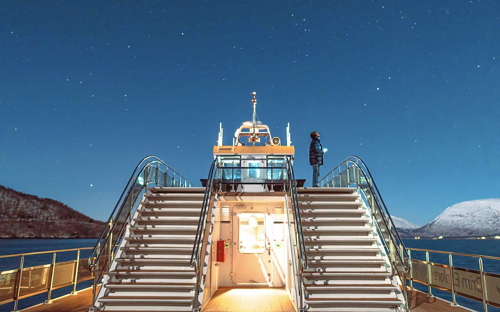 Cruise ship deck under starry sky in Tromso, Norway, with person observing the Northern Lights.