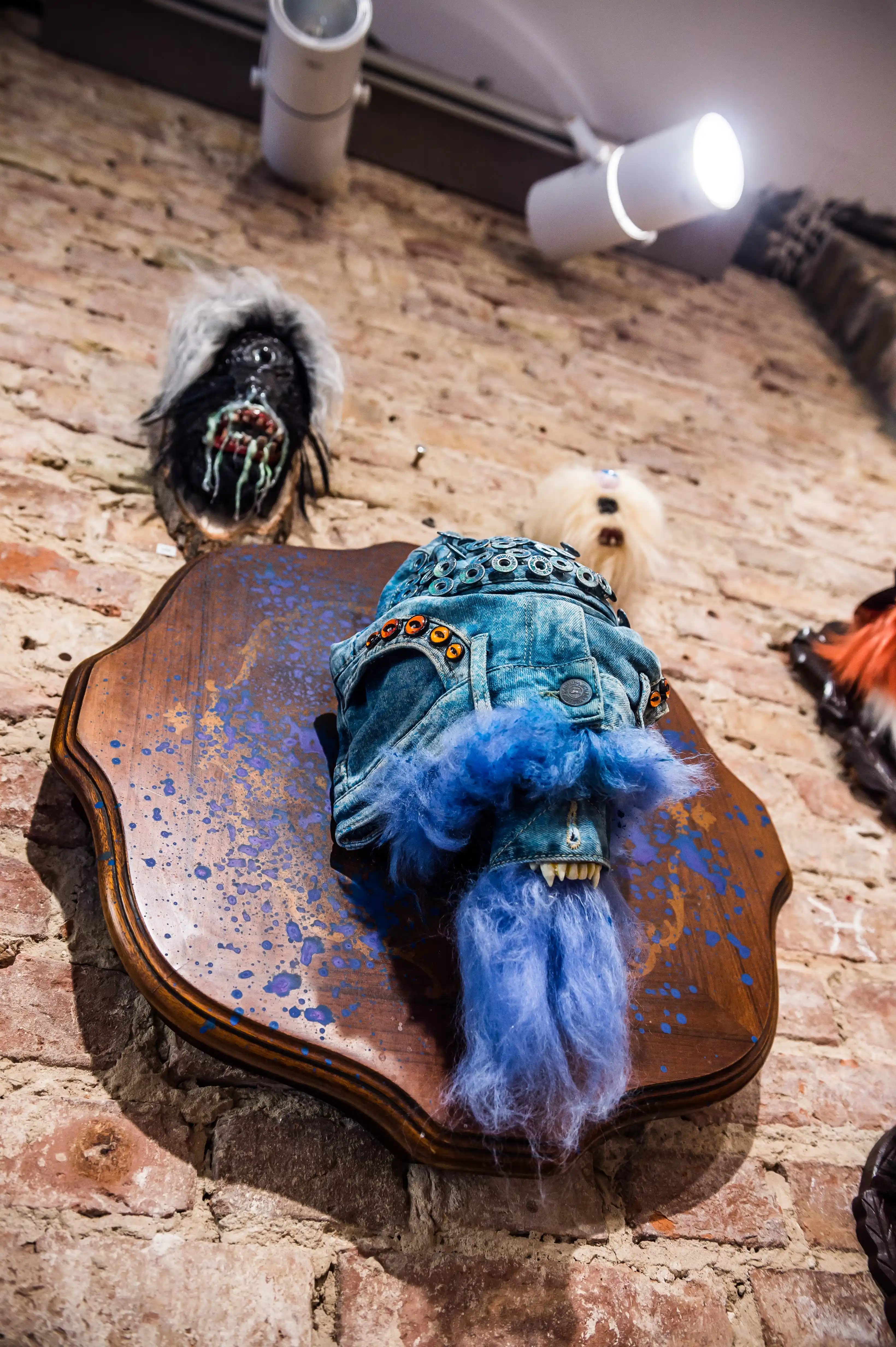 Art installation at the MUSTANG Street ART Lab with studded denim shorts and blue fur mounted on a wooden trophy plaque on a brick wall.