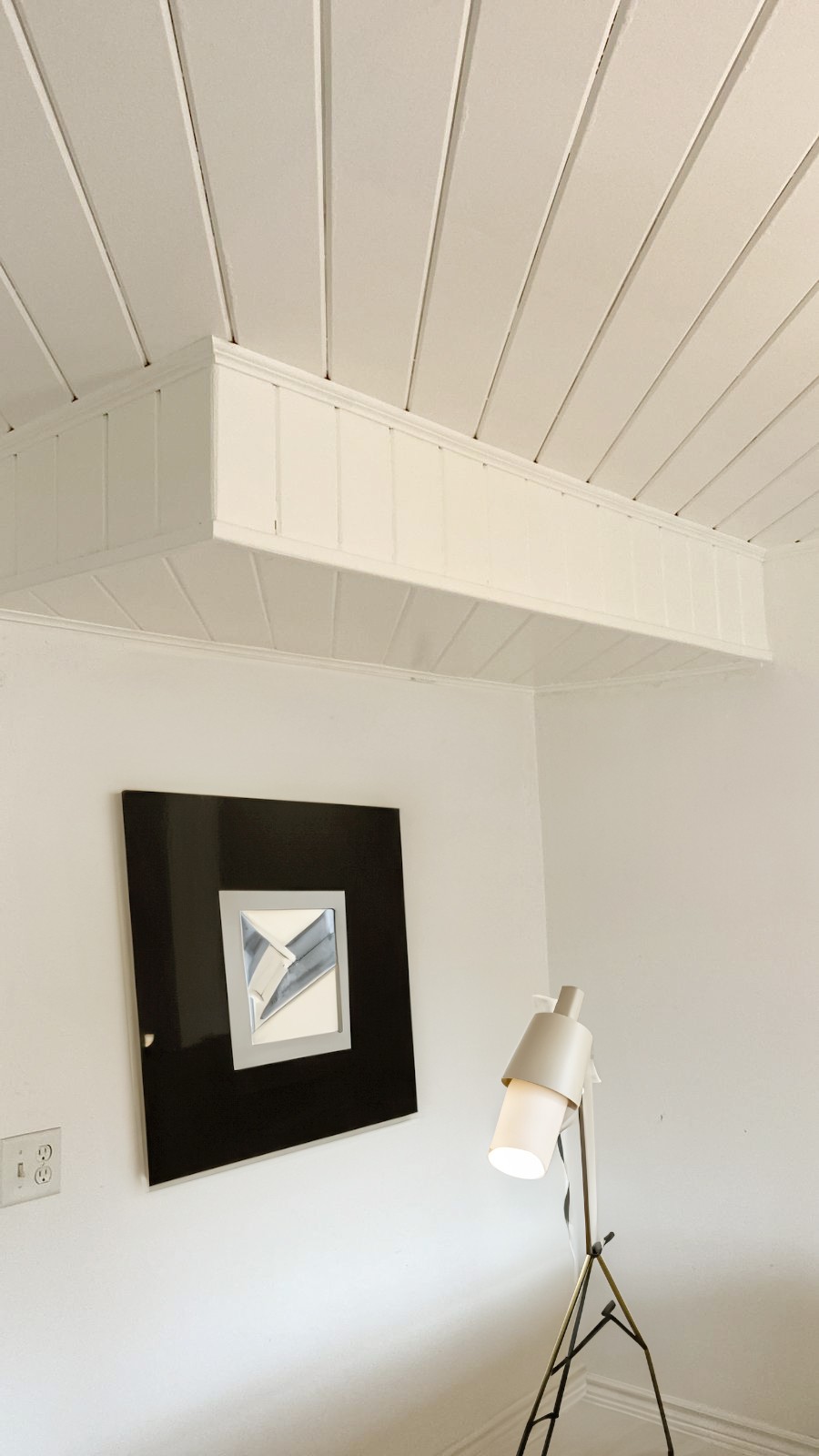 Shiplap ceiling in basement renovation with a mirror on the wall and a floor lamp. 