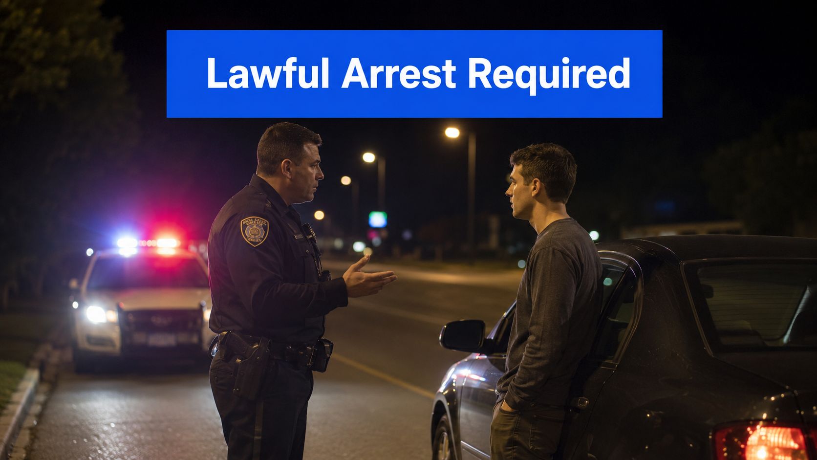 A police officer talks to a young man next to a car with police lights at night.