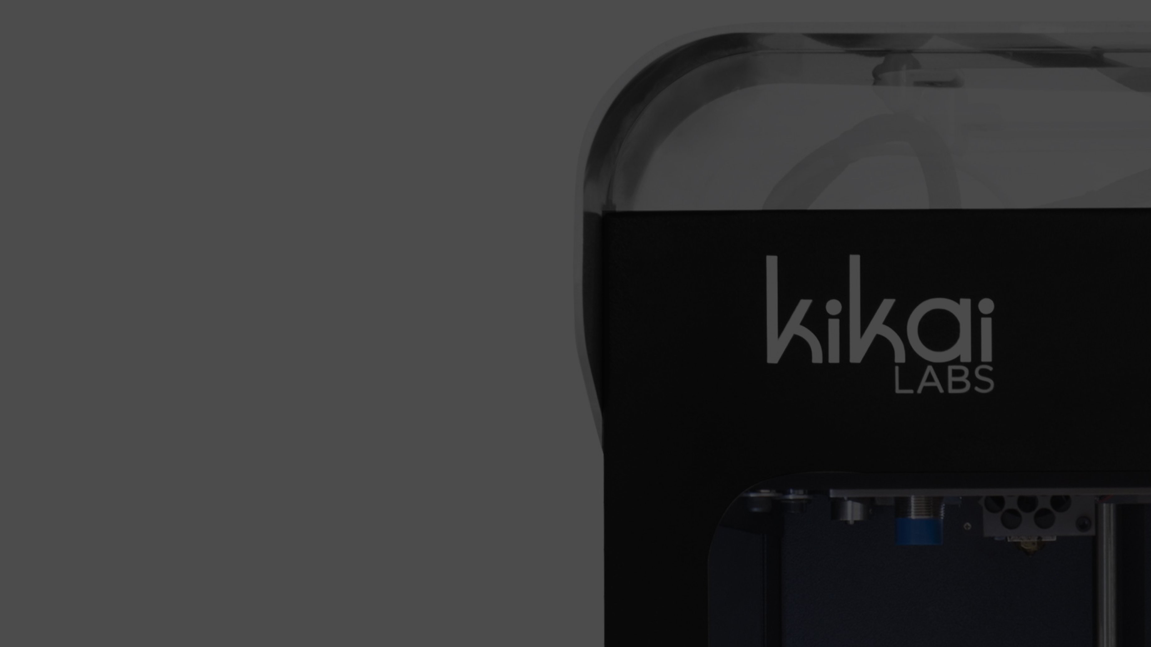 Partial view of a 3D printer with "Kikai Labs" logo on a black frame. The sleek design and dark tones convey a modern, tech-focused atmosphere.