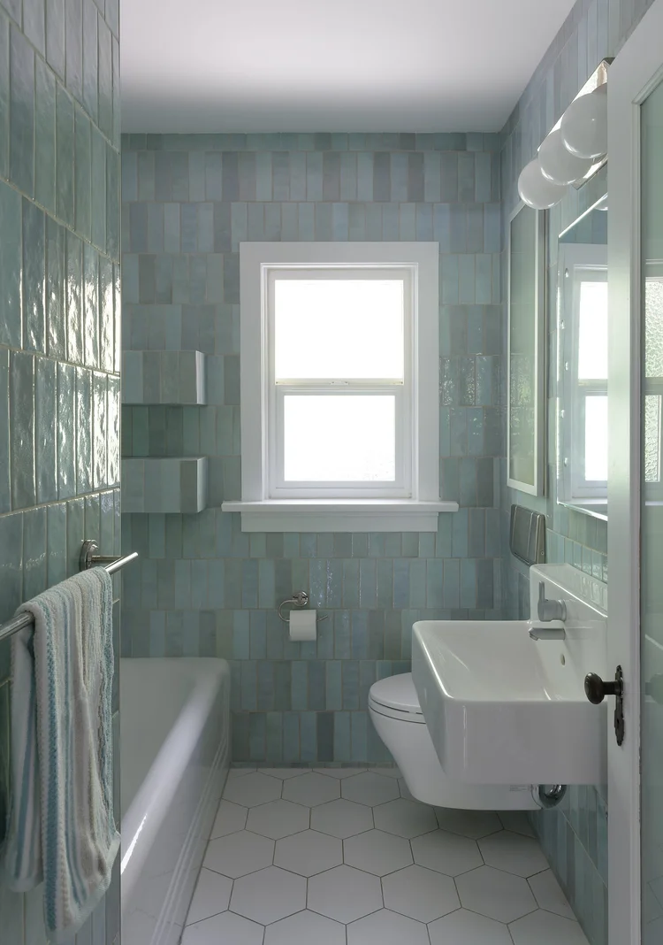 Modern two-story home with large glass windows, warmly lit interiors, and a balcony. Surrounded by trees and a manicured lawn at dusk. Cozy ambiance.