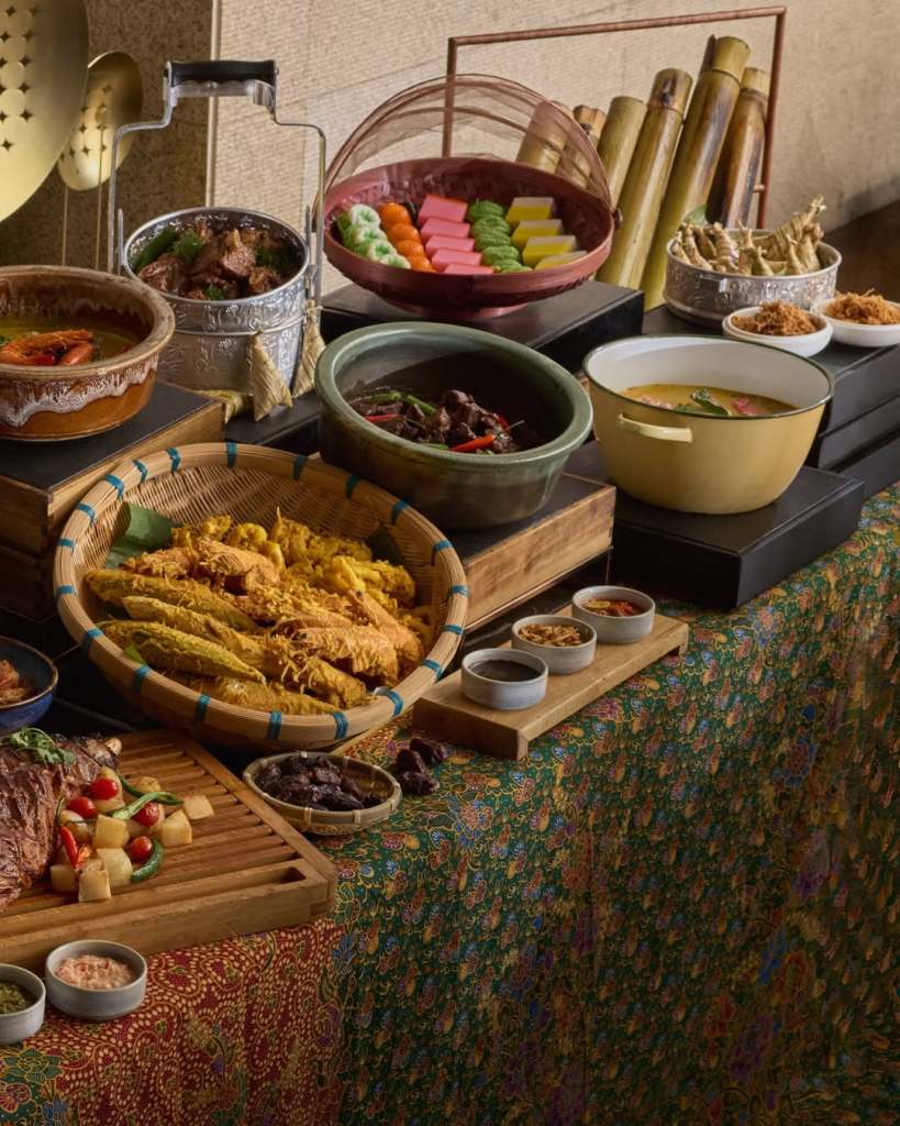 A vibrant display of various traditional dishes including curries, grilled meats, and colorful desserts arranged on a patterned tablecloth.
