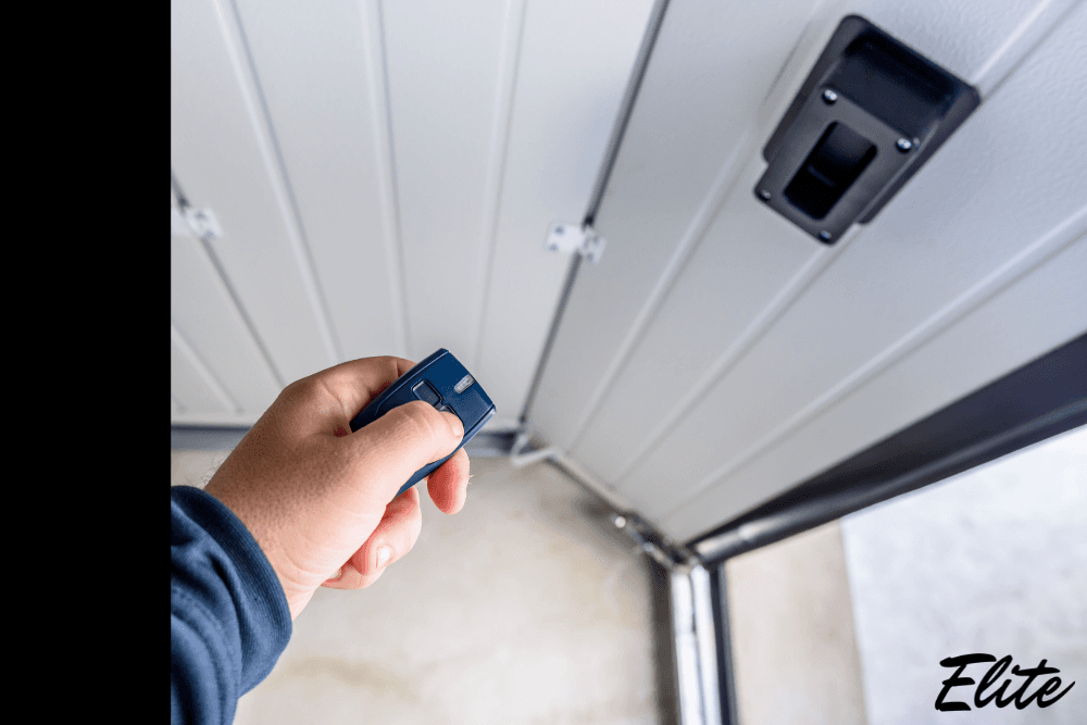 Hand using a remote to open a modern garage door installed by Elite Garage Door in NWA.