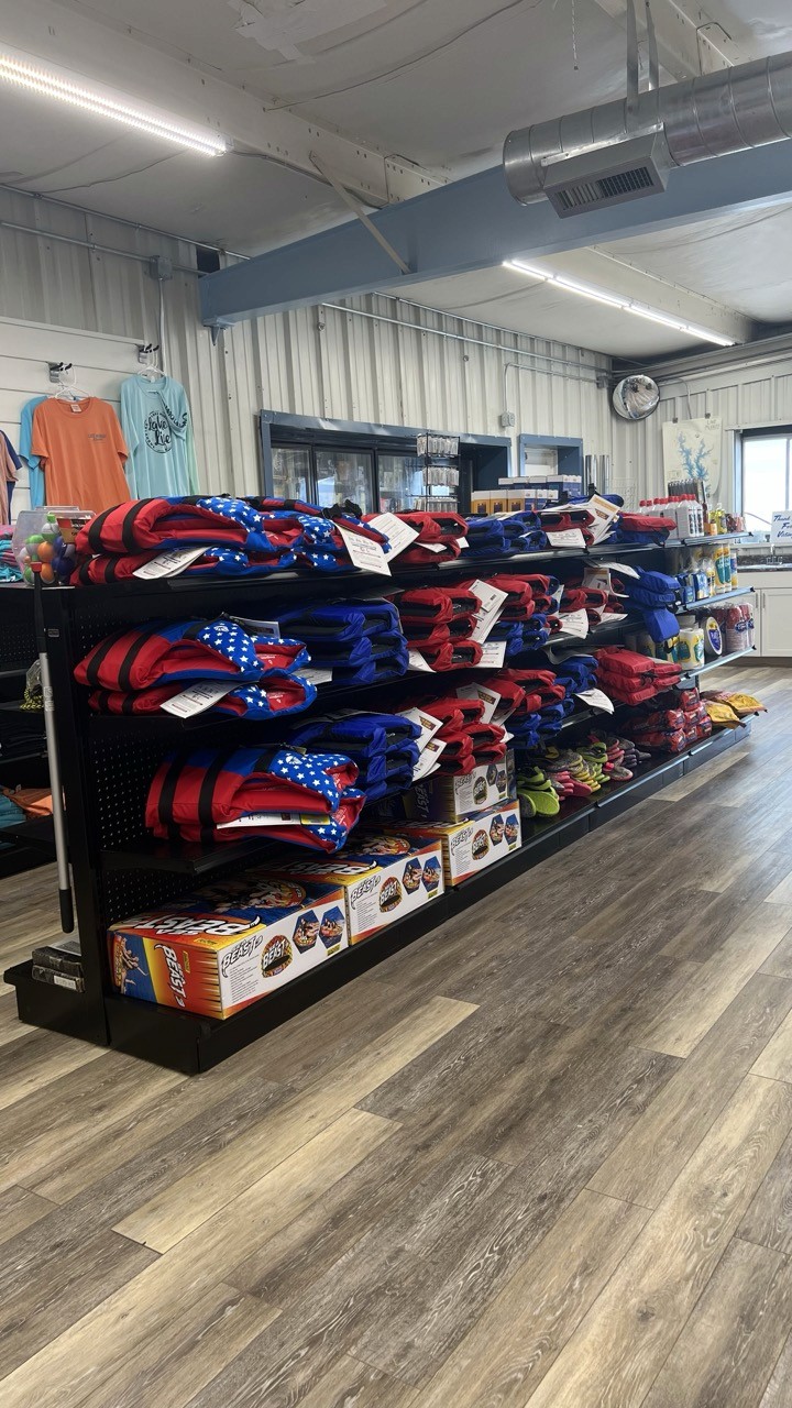 A store aisle featuring neatly stacked shelves displaying colorful life jackets and boxes, with apparel hanging in the background and a wooden floor enhancing the retail display setting.