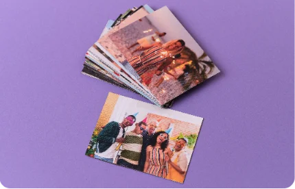 Pessoa segurando foto de casal sorridente em viagem ensolarada, com mesa azul, laranja e suco ao fundo