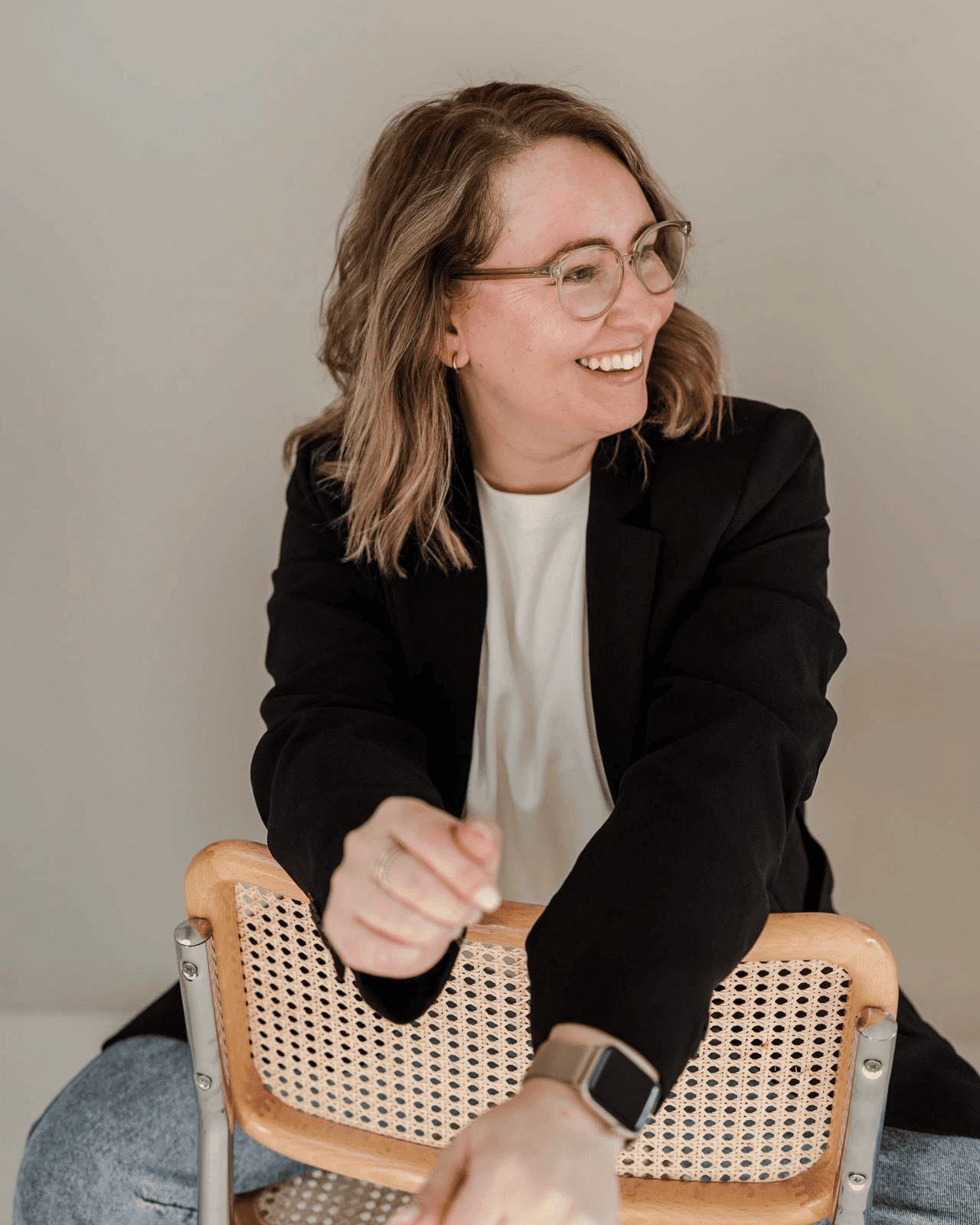 Markenstrategin Sarina von OHNORD studio aus Straubing sitzt auf einem Korbstuhl, mit einem schwarzen Blazer und Jeans. Ihr Lachen ist offen und herzlich, was die Philosophie des Website Unternehmens widerspiegelt. 